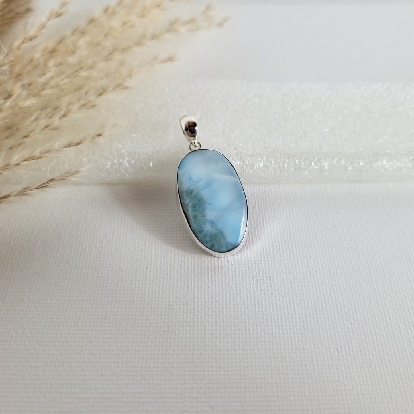 Larimar Kettenanhänger in 925er Silberfassung, 2,6 x 1,7 cm, mit hellblauen und weißen Farbverläufen, fotografiert vor neutralem Hintergrund.