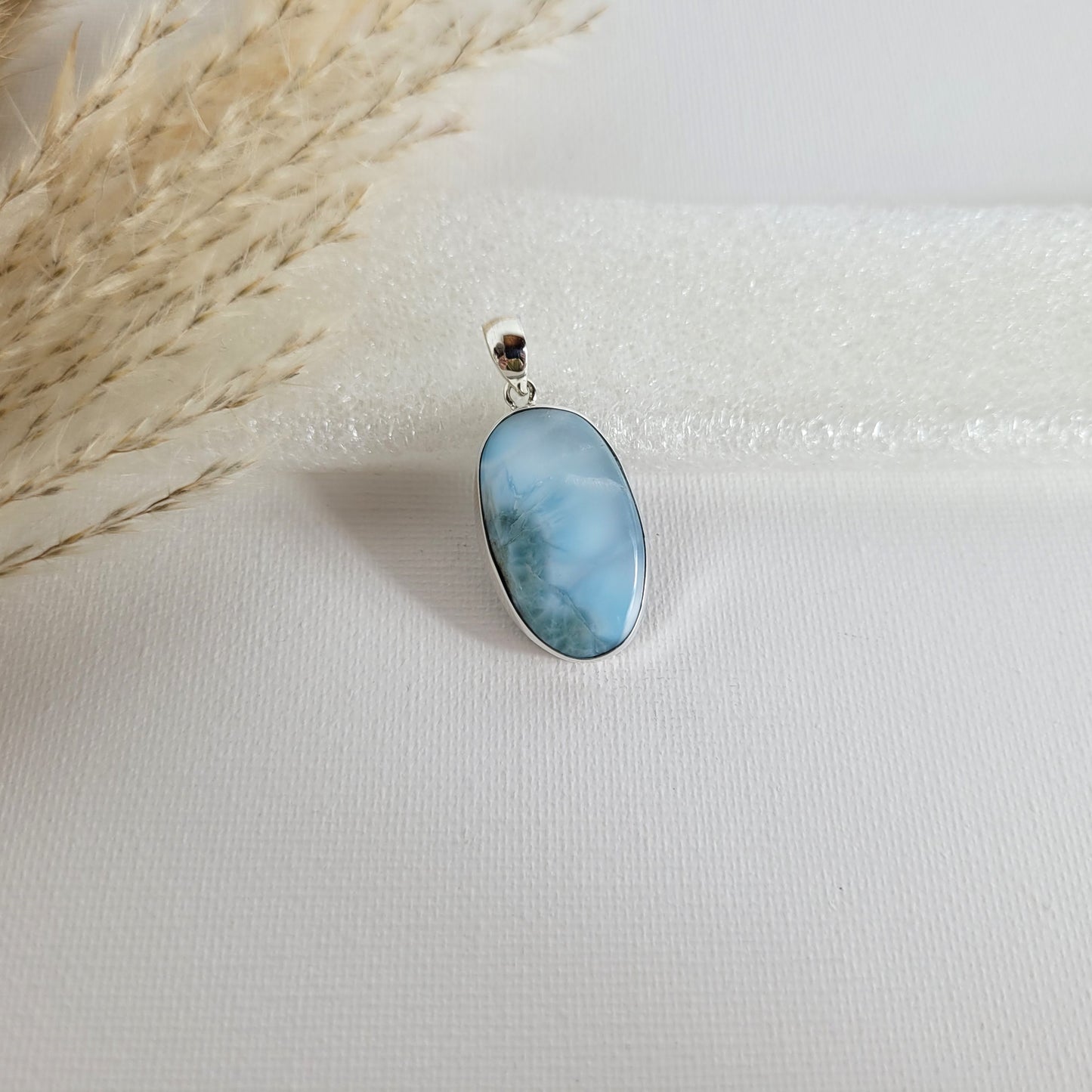 Larimar Kettenanhänger in 925er Silberfassung, 2,6 x 1,7 cm, mit hellblauen und weißen Farbverläufen, fotografiert vor neutralem Hintergrund.