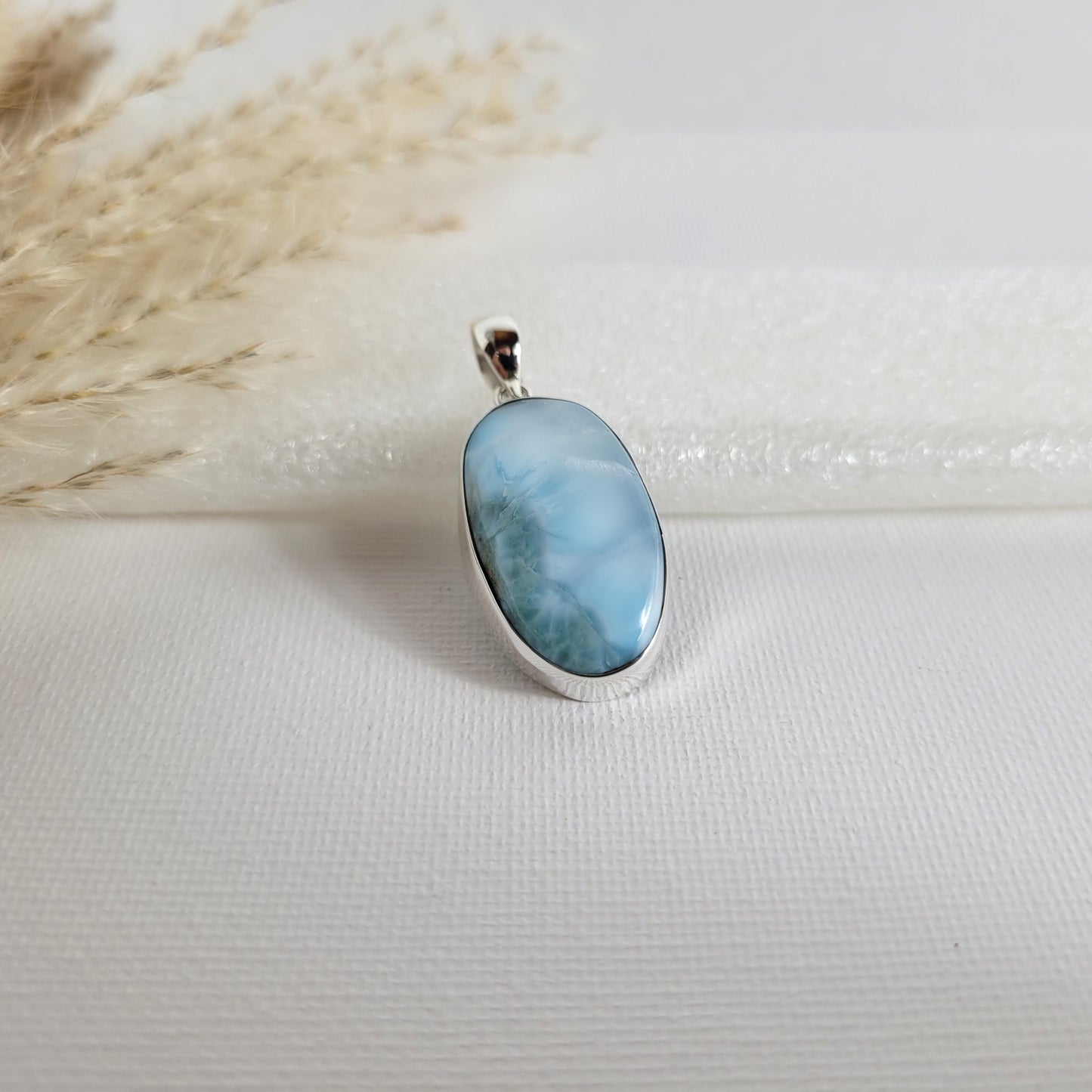Larimar Kettenanhänger in 925er Silberfassung, 2,6 x 1,7 cm, mit hellblauen und weißen Farbverläufen, fotografiert vor neutralem Hintergrund.