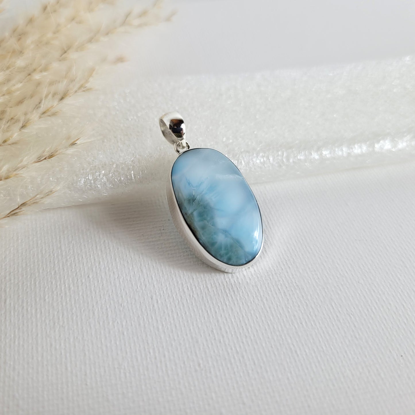 Larimar Kettenanhänger in 925er Silberfassung, 2,6 x 1,7 cm, mit hellblauen und weißen Farbverläufen, fotografiert vor neutralem Hintergrund.