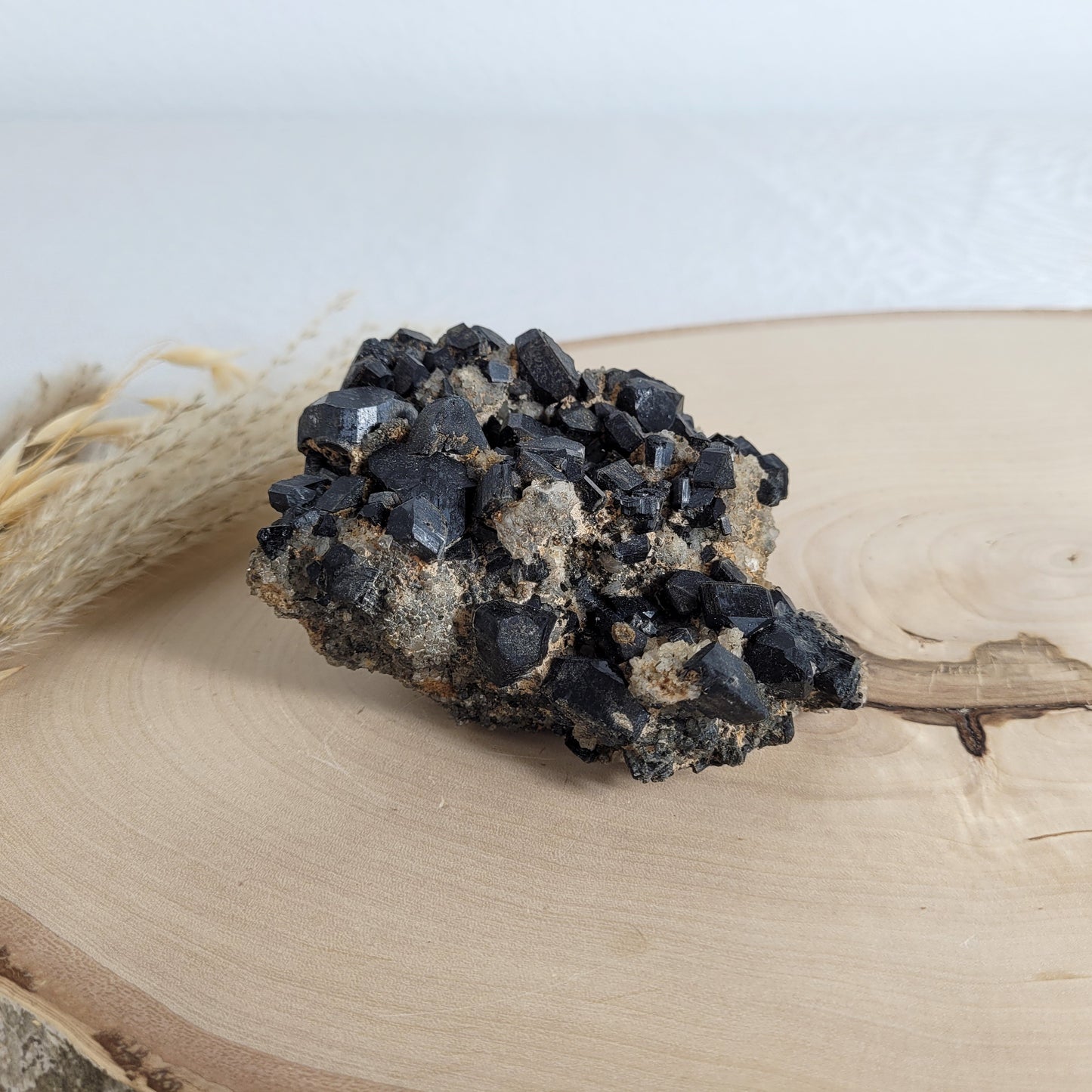 Seltene Kristallstufe mit würfelförmigen schwarzen Turmalin-Kristallen auf Quarzgestein, Größe 10,3 x 7,1 cm, fotografiert auf einer Holzscheibe.