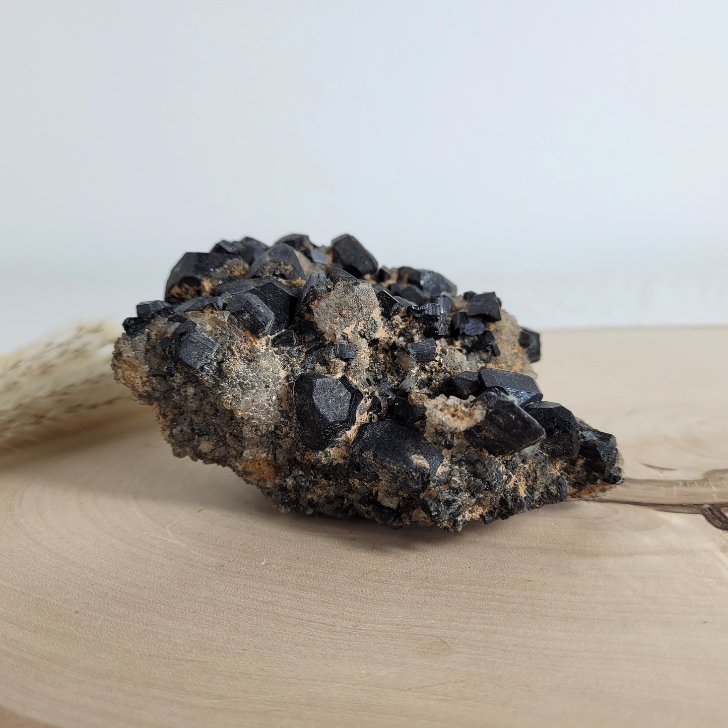 Seltene Kristallstufe mit würfelförmigen schwarzen Turmalin-Kristallen auf Quarzgestein, Größe 10,3 x 7,1 cm, fotografiert auf einer Holzscheibe.