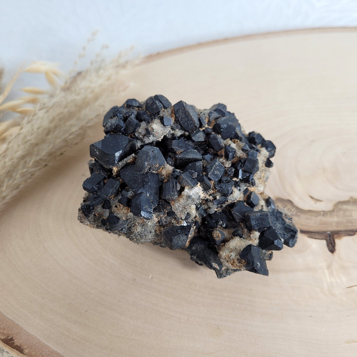Seltene Kristallstufe mit würfelförmigen schwarzen Turmalin-Kristallen auf Quarzgestein, Größe 10,3 x 7,1 cm, fotografiert auf einer Holzscheibe.