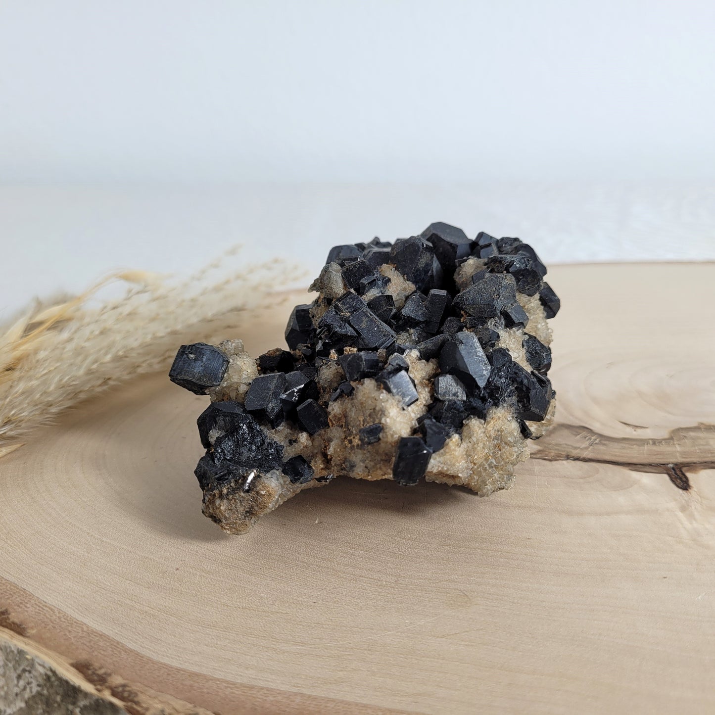 Seltene Kristallstufe mit würfelförmigen schwarzen Turmalin-Kristallen auf Quarzgestein, Größe 10,3 x 7,1 cm, fotografiert auf einer Holzscheibe.