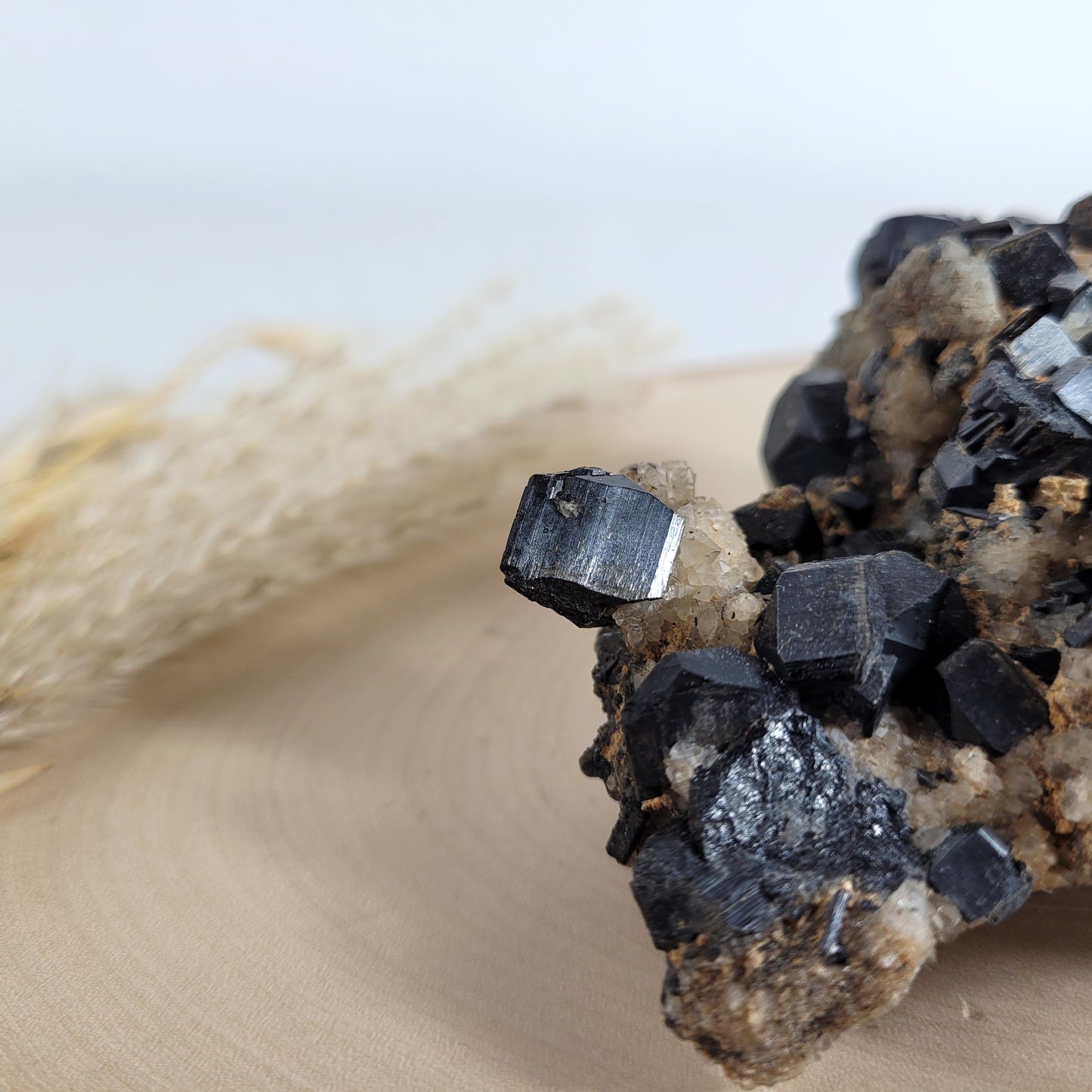 Seltene Kristallstufe mit würfelförmigen schwarzen Turmalin-Kristallen auf Quarzgestein, Größe 10,3 x 7,1 cm, fotografiert auf einer Holzscheibe.