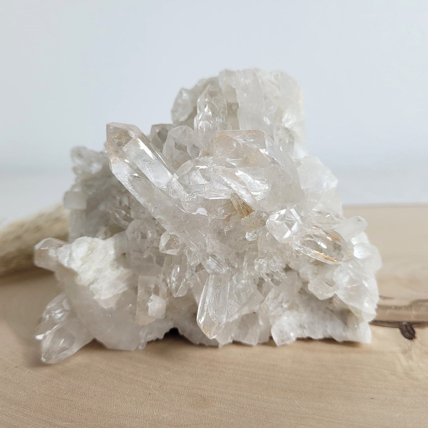 Bergkristall Naturstufe mit klaren Kristallen, platziert auf einer Holzscheibe, neutraler Hintergrund.