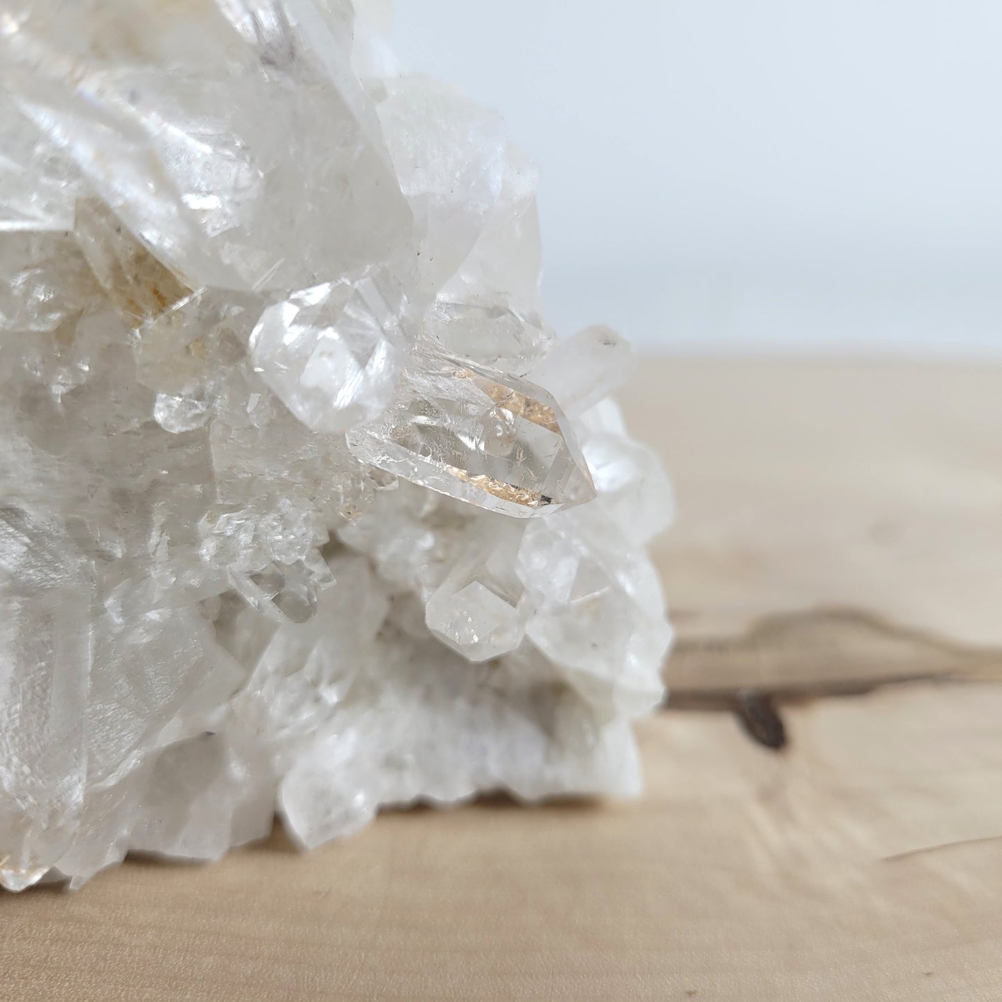 Bergkristall Naturstufe mit klaren Kristallen, platziert auf einer Holzscheibe, neutraler Hintergrund.