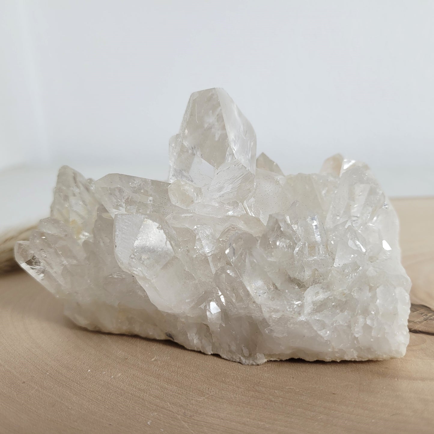 Bergkristall Naturstufe mit klaren Kristallen, platziert auf einer Holzscheibe, neutraler Hintergrund.