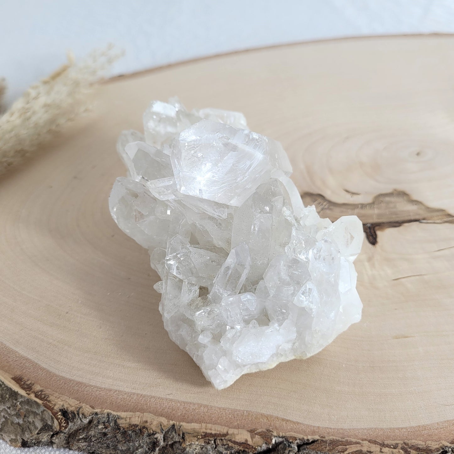Bergkristall Naturstufe mit klaren Kristallen, platziert auf einer Holzscheibe, neutraler Hintergrund.