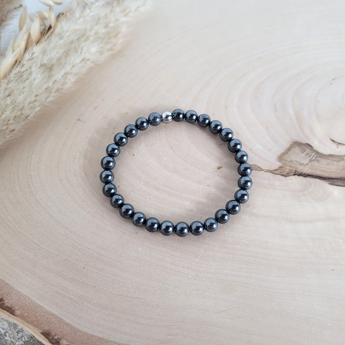 Elastisches Armband mit 6 mm Hämatit Perlen und Edelstahl Endperle, Holzscheibe als Hintergrund.