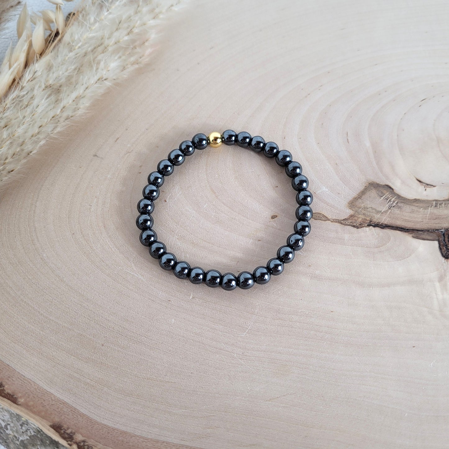 Elastisches Armband mit 6 mm Hämatit Perlen und Silber 925 vergoldeter Endperle, Holzscheibe als Hintergrund.