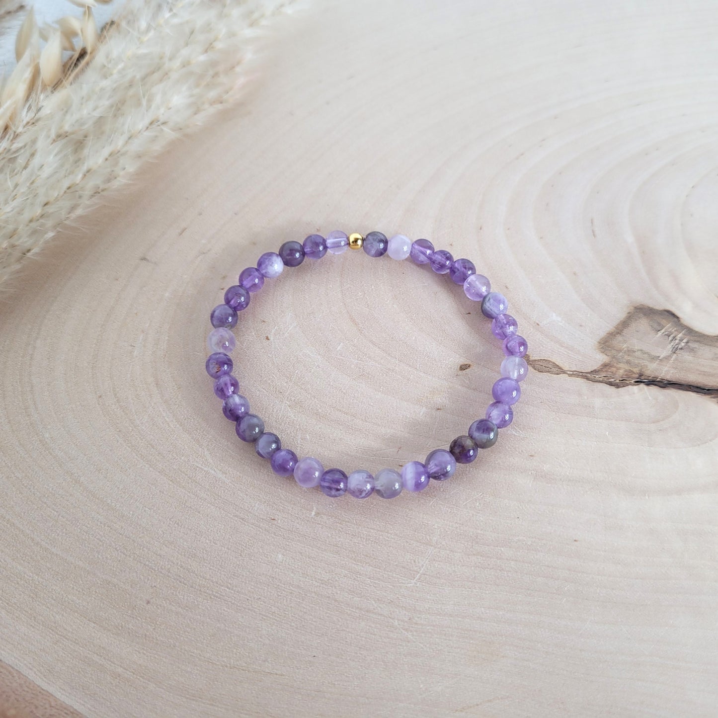 Elastisches Armband mit 5 mm Amethyst Perlen und Silber 925 vergoldeter Endperle, Holzscheibe als Hintergrund.