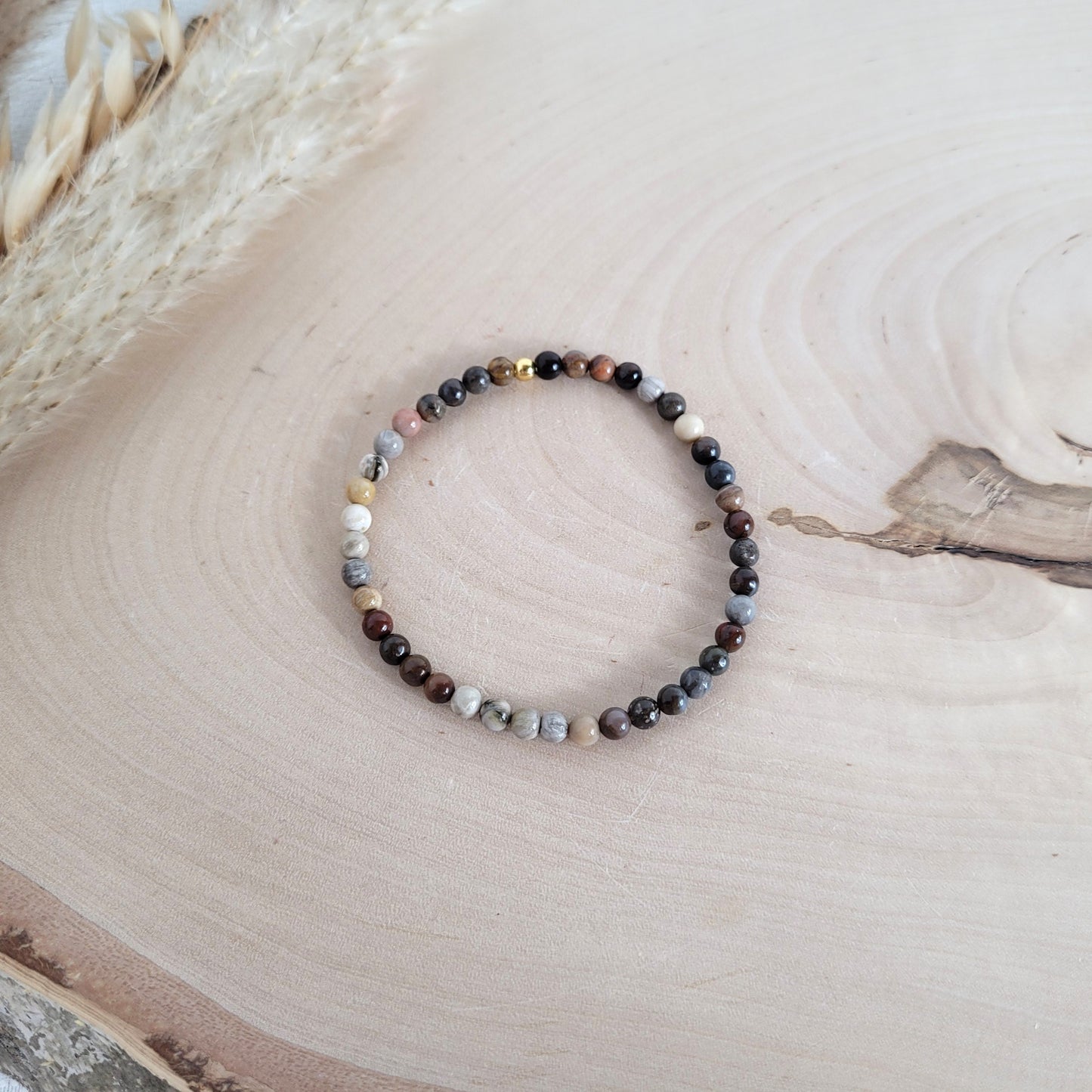 Elastisches Armband mit 4 mm Versteinertes Holz Perlen und Silber 925 vergoldeter Endperle, Holzscheibe als Hintergrund.