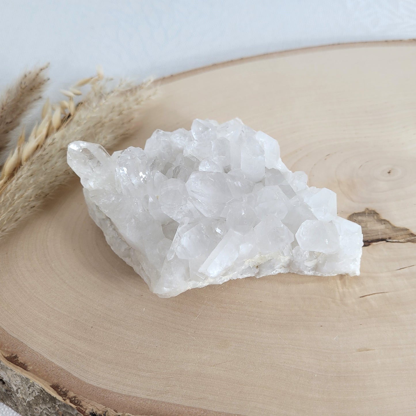 Bergkristall Naturstufe mit klaren Kristallen, platziert auf einer Holzscheibe, neutraler Hintergrund.