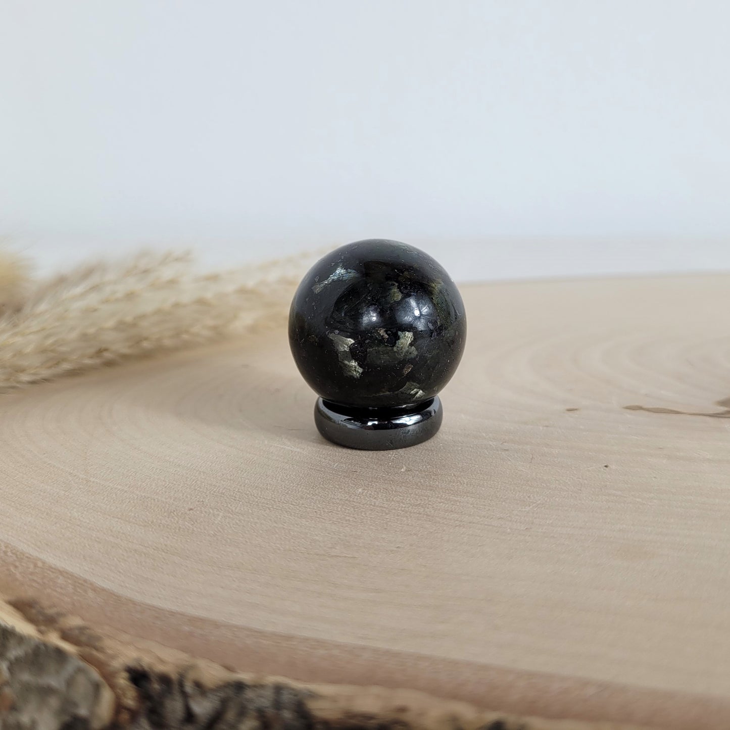 Polierte Larvikit Kugel mit 3 cm Durchmesser, bläulicher Schimmer auf dunklem Gestein, platziert auf einer Holzscheibe.