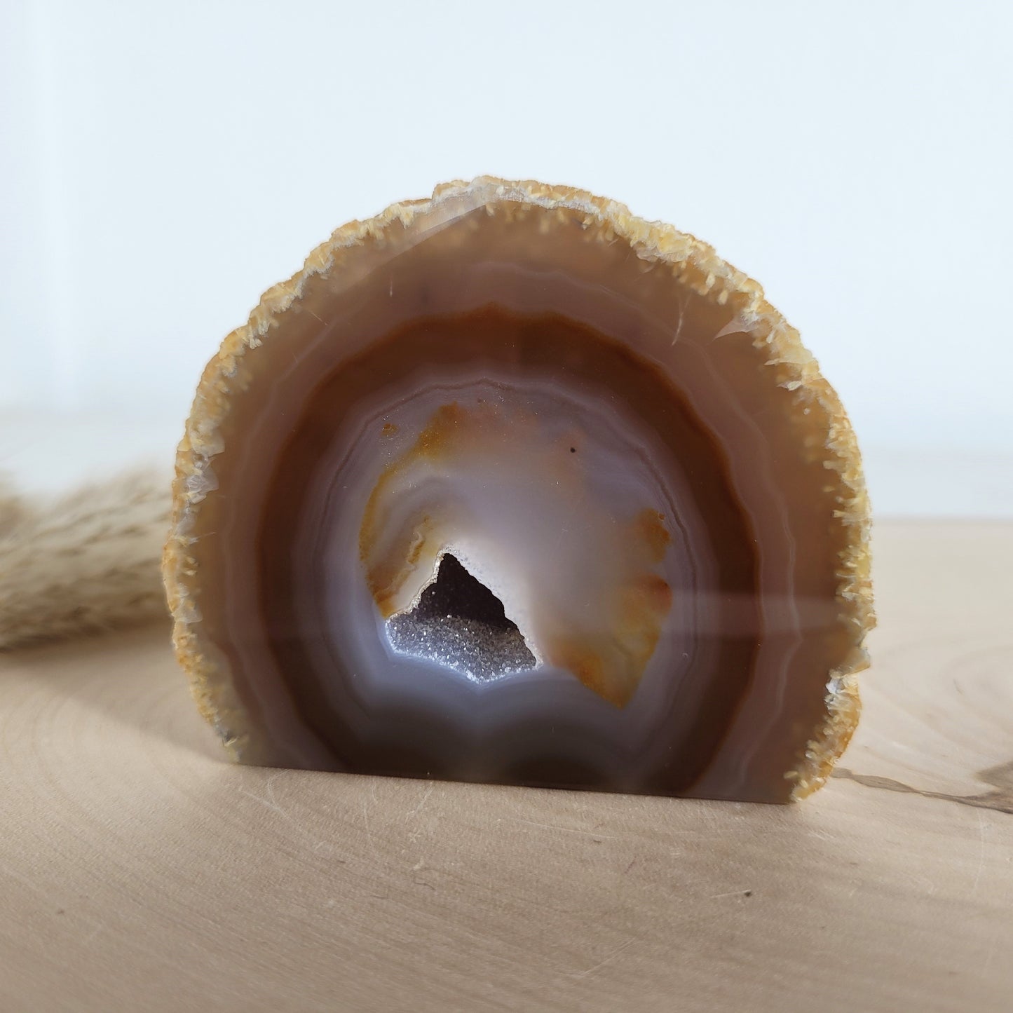 Achat Geode mit natürlicher Kristallöffnung und flacher Standfläche, platziert auf einer Holzscheibe.