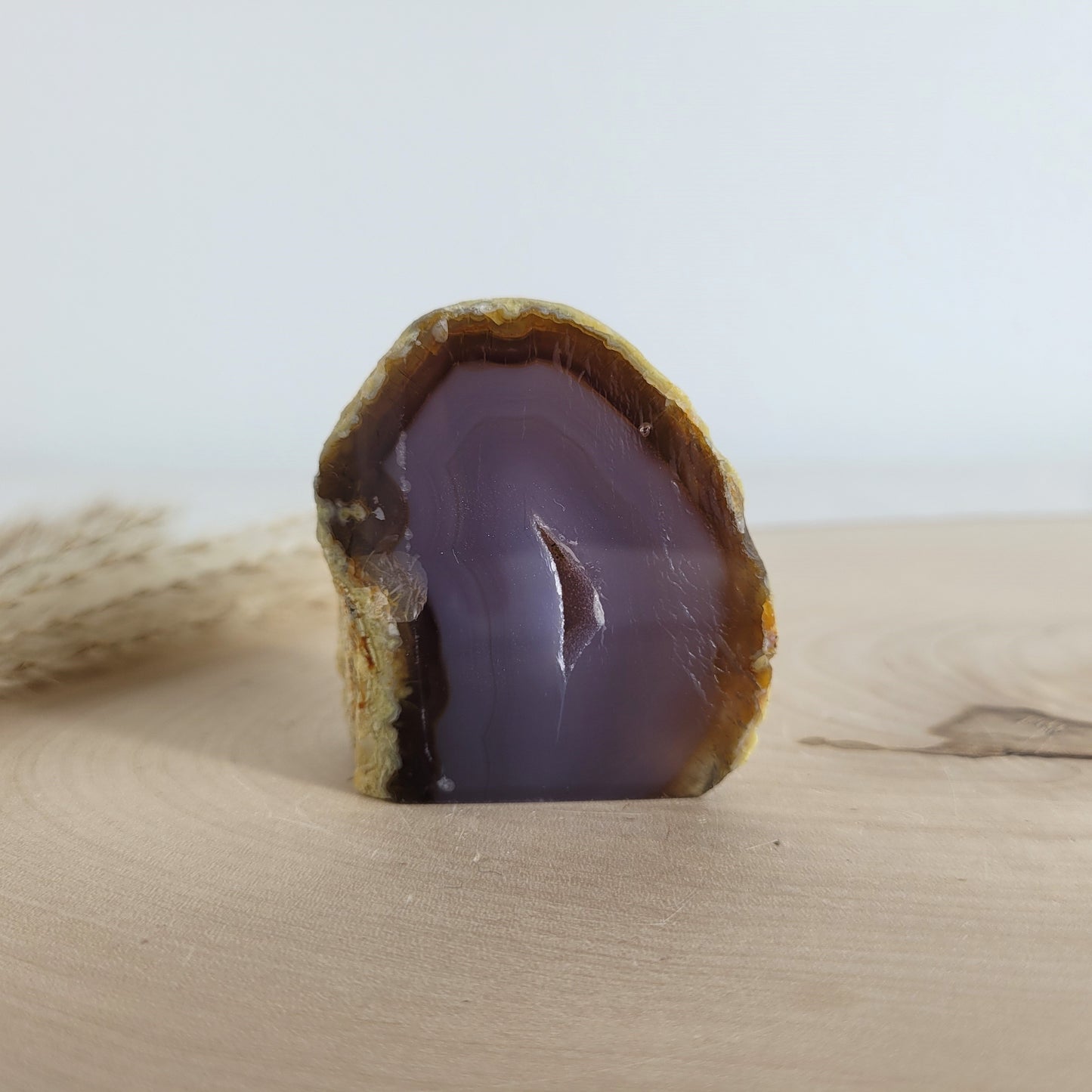 Achat Geode mit natürlicher Kristallöffnung und flacher Standfläche, platziert auf einer Holzscheibe.