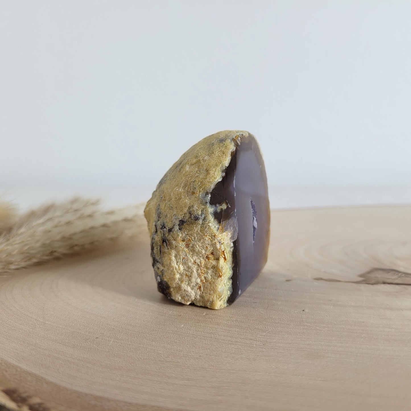 Achat Geode mit natürlicher Kristallöffnung und flacher Standfläche, platziert auf einer Holzscheibe.