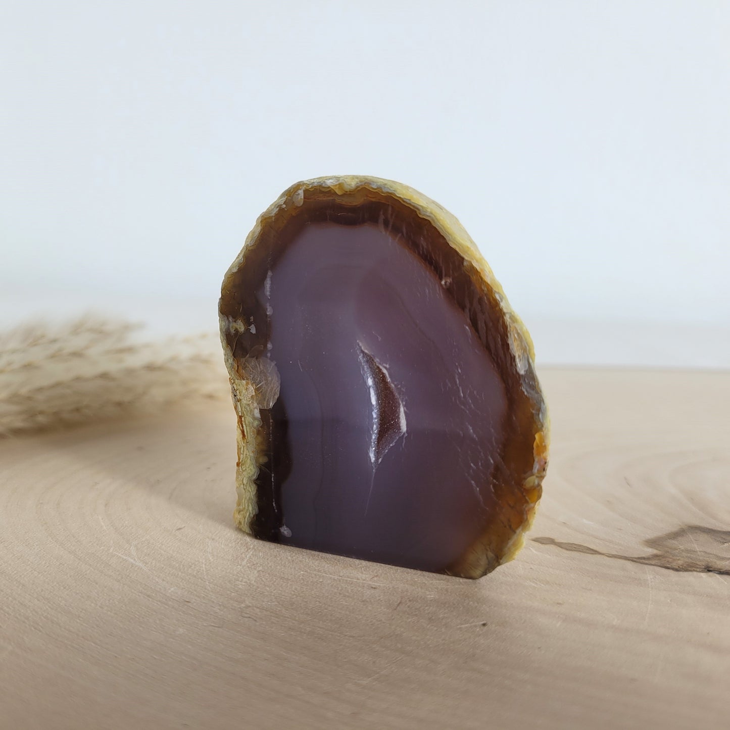 Achat Geode mit natürlicher Kristallöffnung und flacher Standfläche, platziert auf einer Holzscheibe.