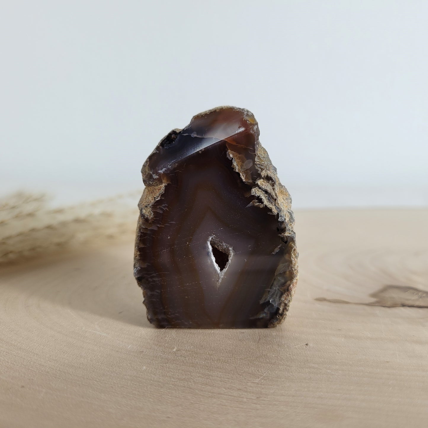 Achat Geode mit natürlicher Kristallöffnung und flacher Standfläche, platziert auf einer Holzscheibe.
