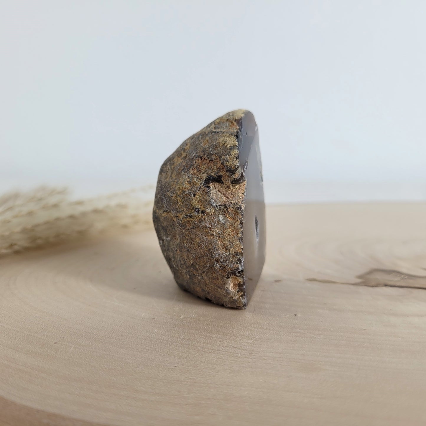 Achat Geode mit natürlicher Kristallöffnung und flacher Standfläche, platziert auf einer Holzscheibe.