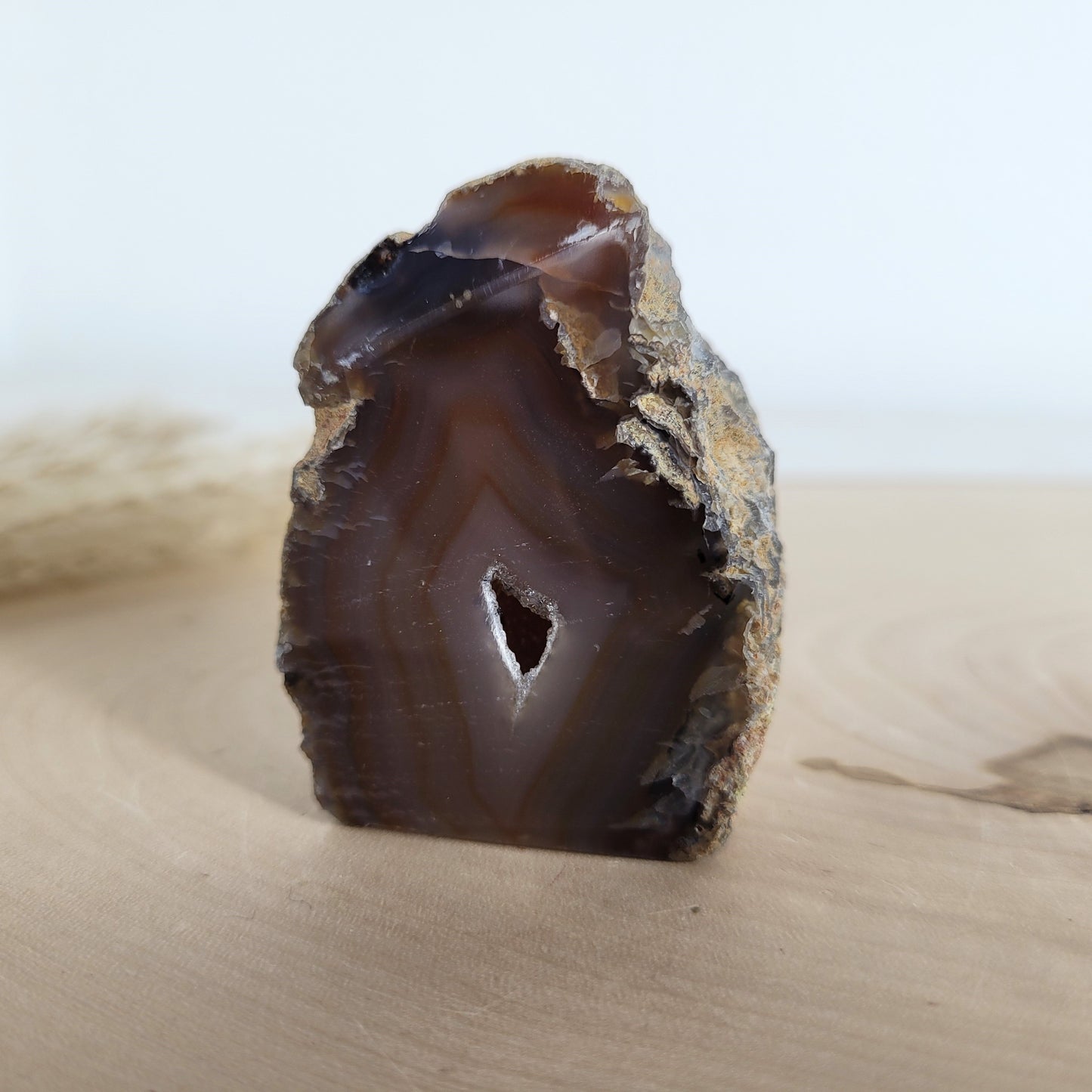Achat Geode mit natürlicher Kristallöffnung und flacher Standfläche, platziert auf einer Holzscheibe.