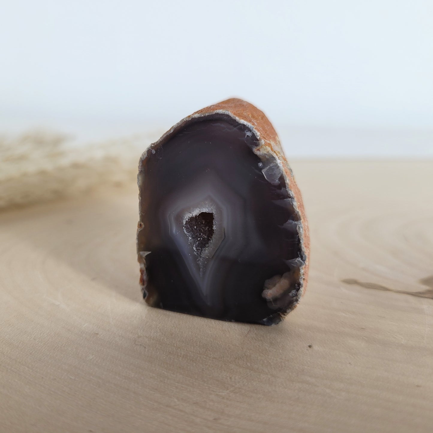 Achat Geode mit natürlicher Kristallöffnung und flacher Standfläche, platziert auf einer Holzscheibe.