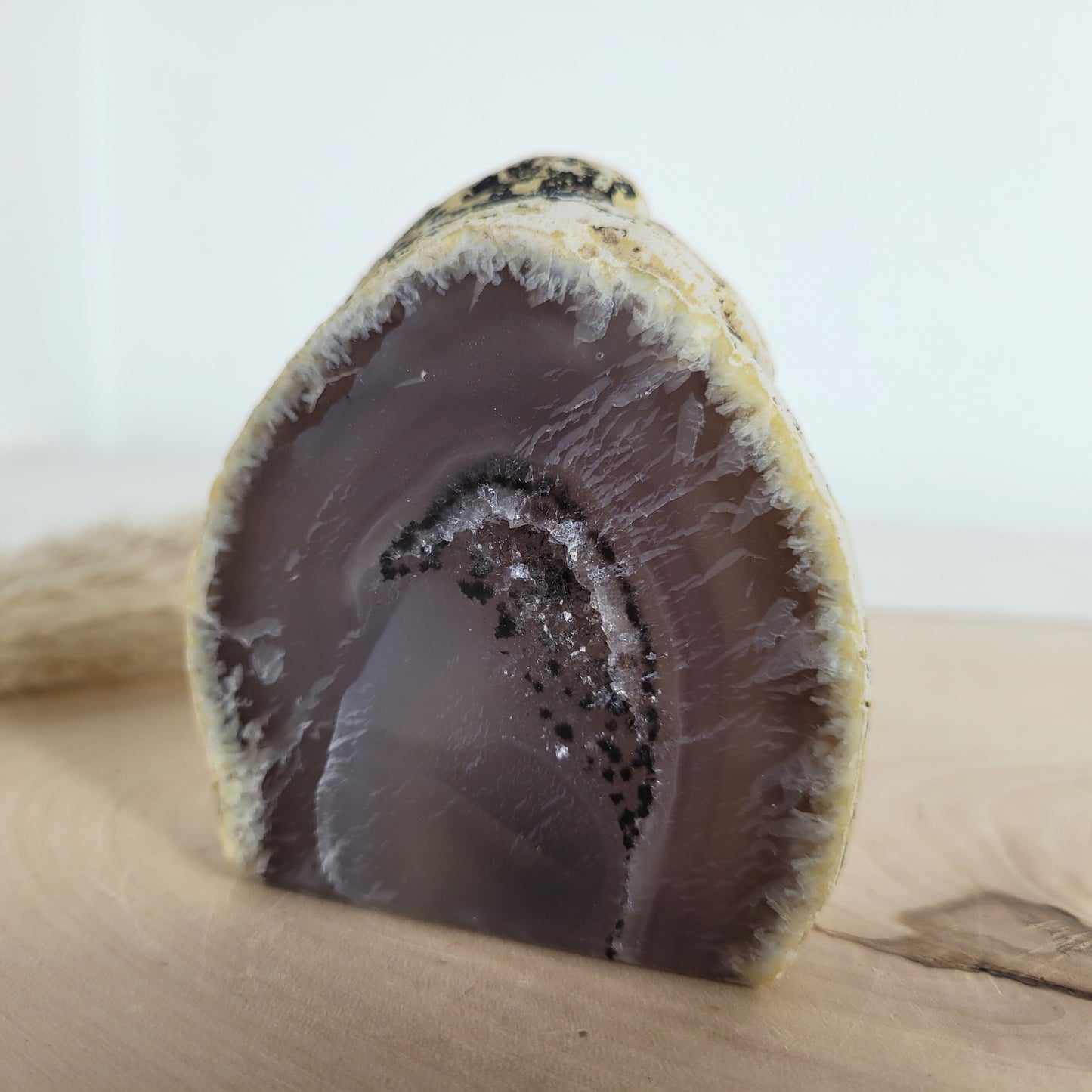 Achat Geode mit natürlicher Kristallöffnung und flacher Standfläche, platziert auf einer Holzscheibe.