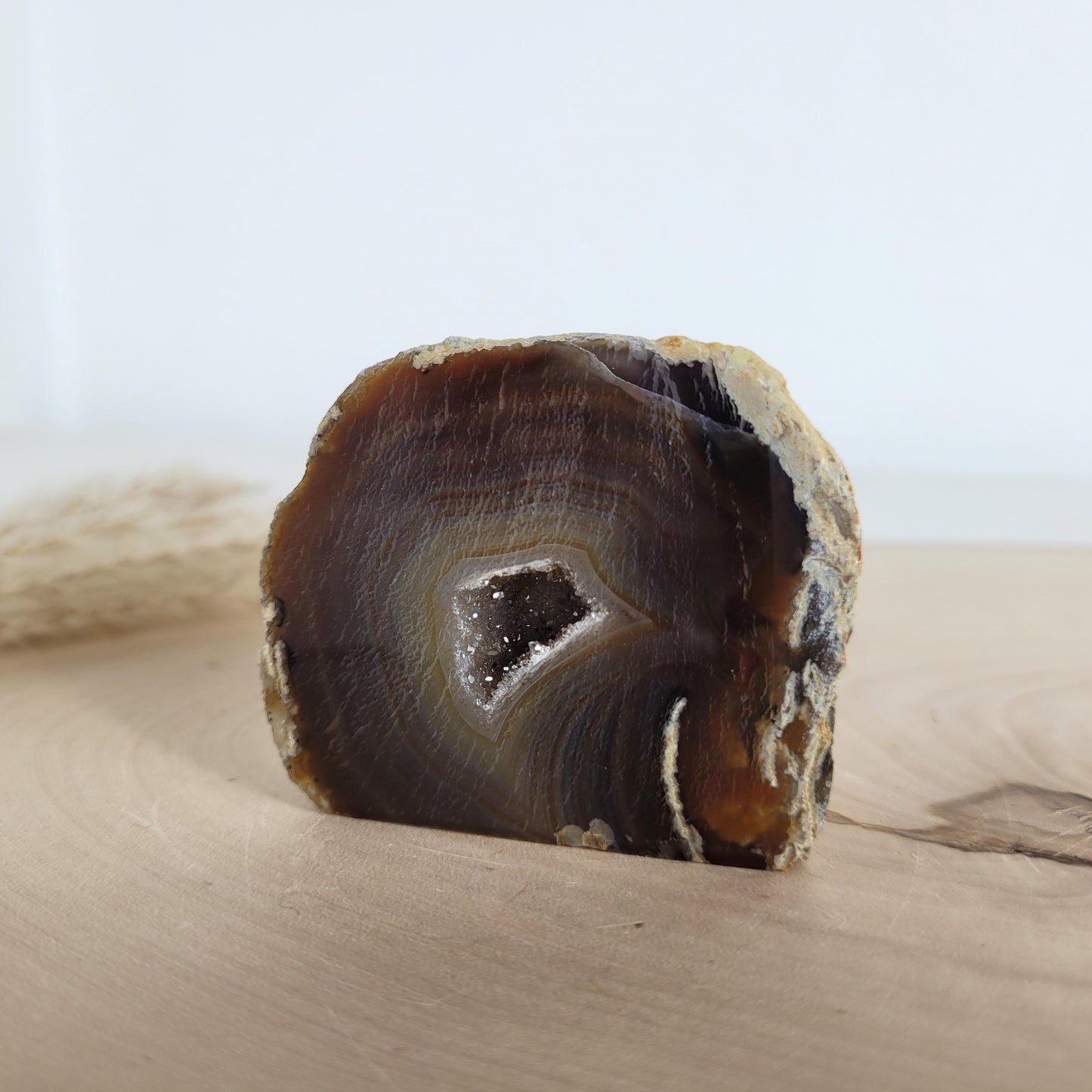 Achat Geode mit natürlicher Kristallöffnung und flacher Standfläche, platziert auf einer Holzscheibe.
