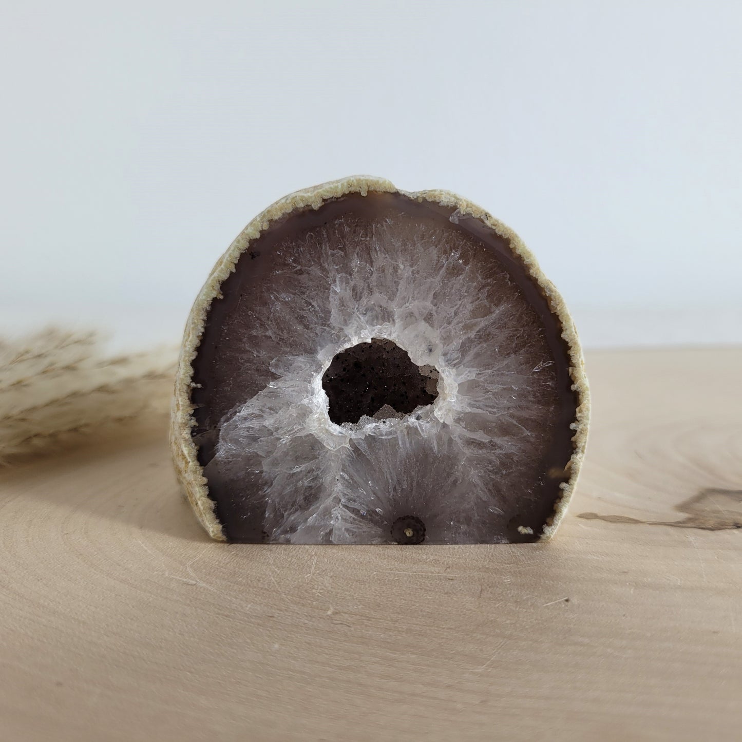 Achat Geode mit natürlicher Kristallöffnung und flacher Standfläche, platziert auf einer Holzscheibe.