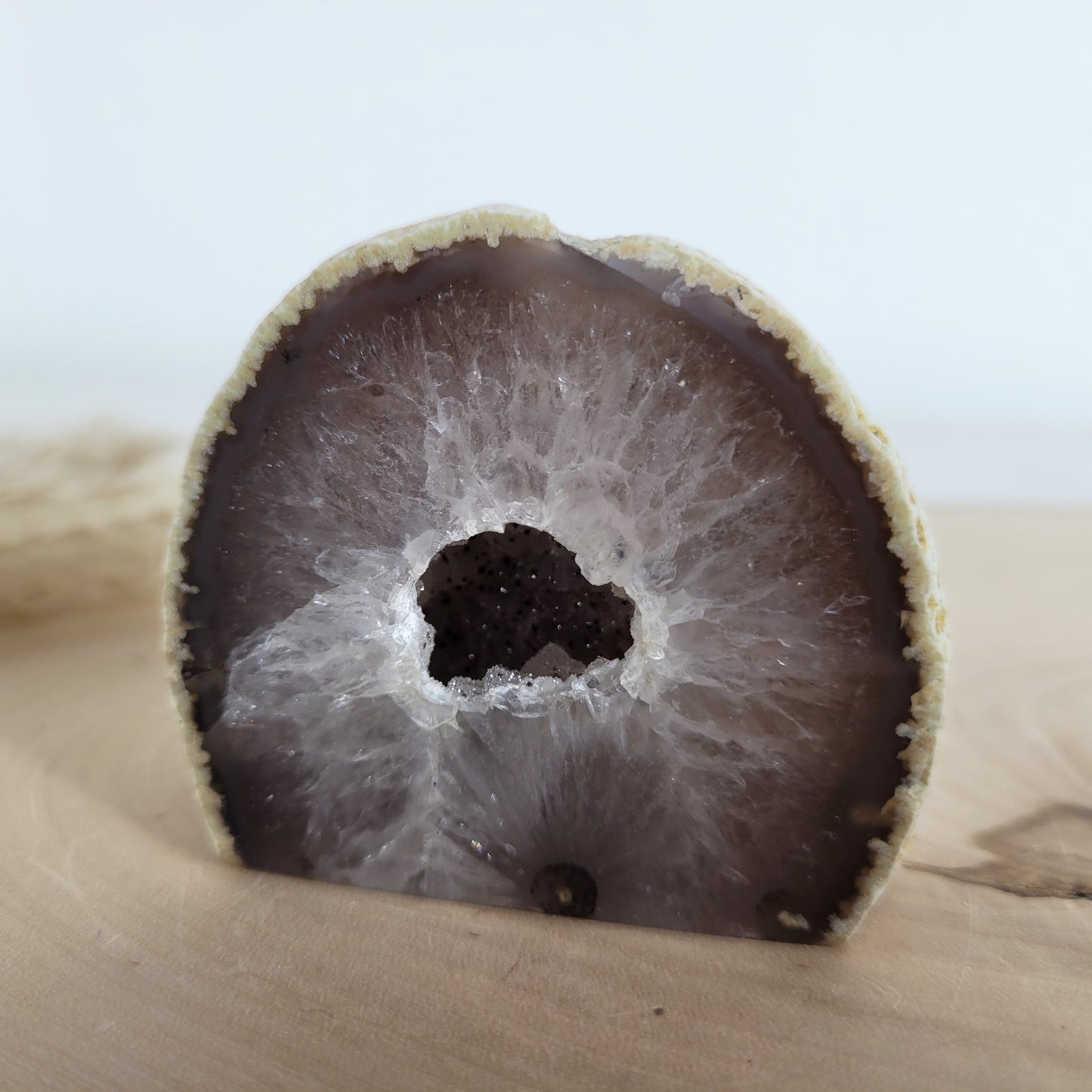 Achat Geode mit natürlicher Kristallöffnung und flacher Standfläche, platziert auf einer Holzscheibe.