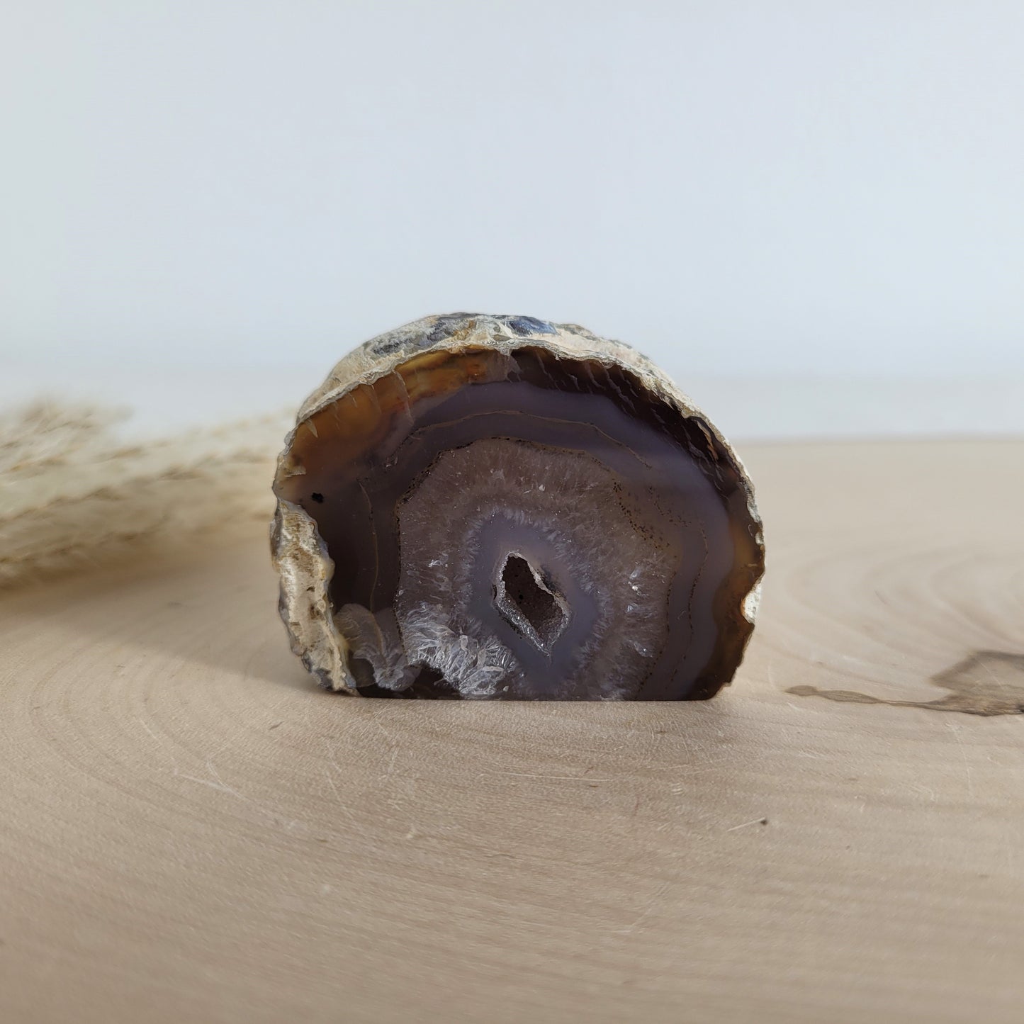 Achat Geode mit natürlicher Kristallöffnung und flacher Standfläche, platziert auf einer Holzscheibe.