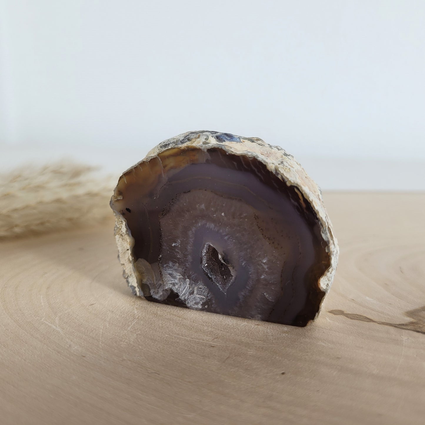 Achat Geode mit natürlicher Kristallöffnung und flacher Standfläche, platziert auf einer Holzscheibe.