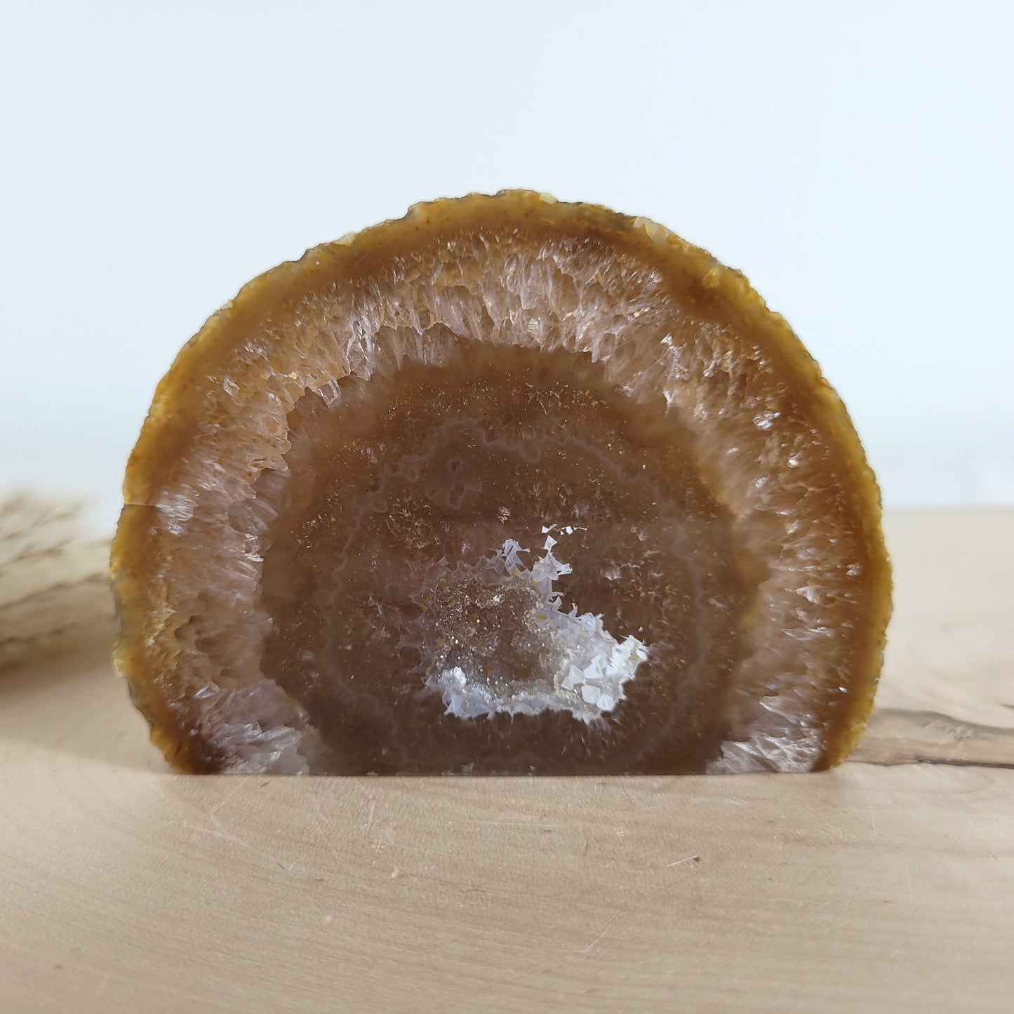 Achat Geode mit natürlicher Kristallöffnung und flacher Standfläche, platziert auf einer Holzscheibe.