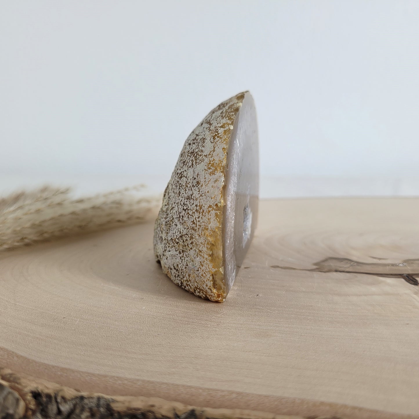 Achat Geode mit natürlicher Kristallöffnung und flacher Standfläche, platziert auf einer Holzscheibe.