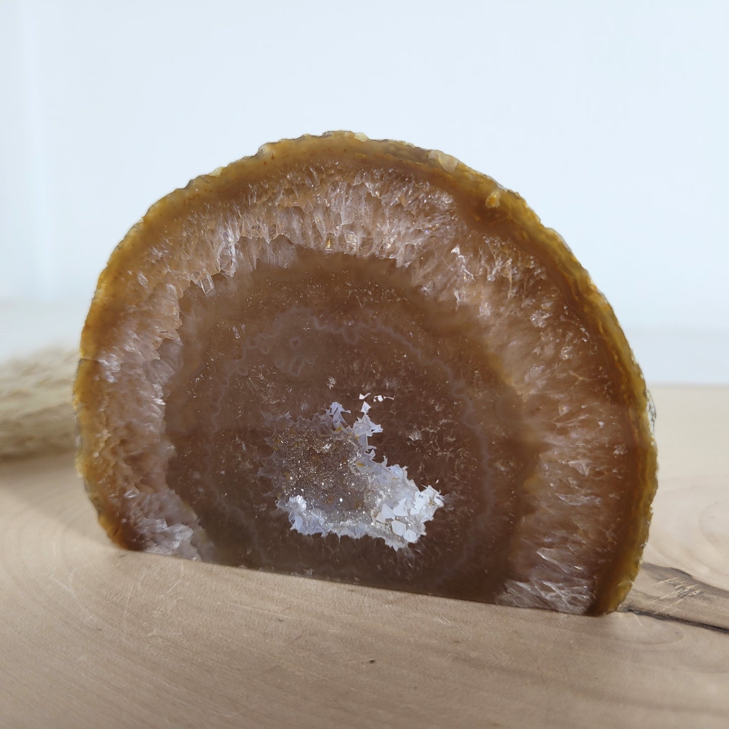 Achat Geode mit natürlicher Kristallöffnung und flacher Standfläche, platziert auf einer Holzscheibe.