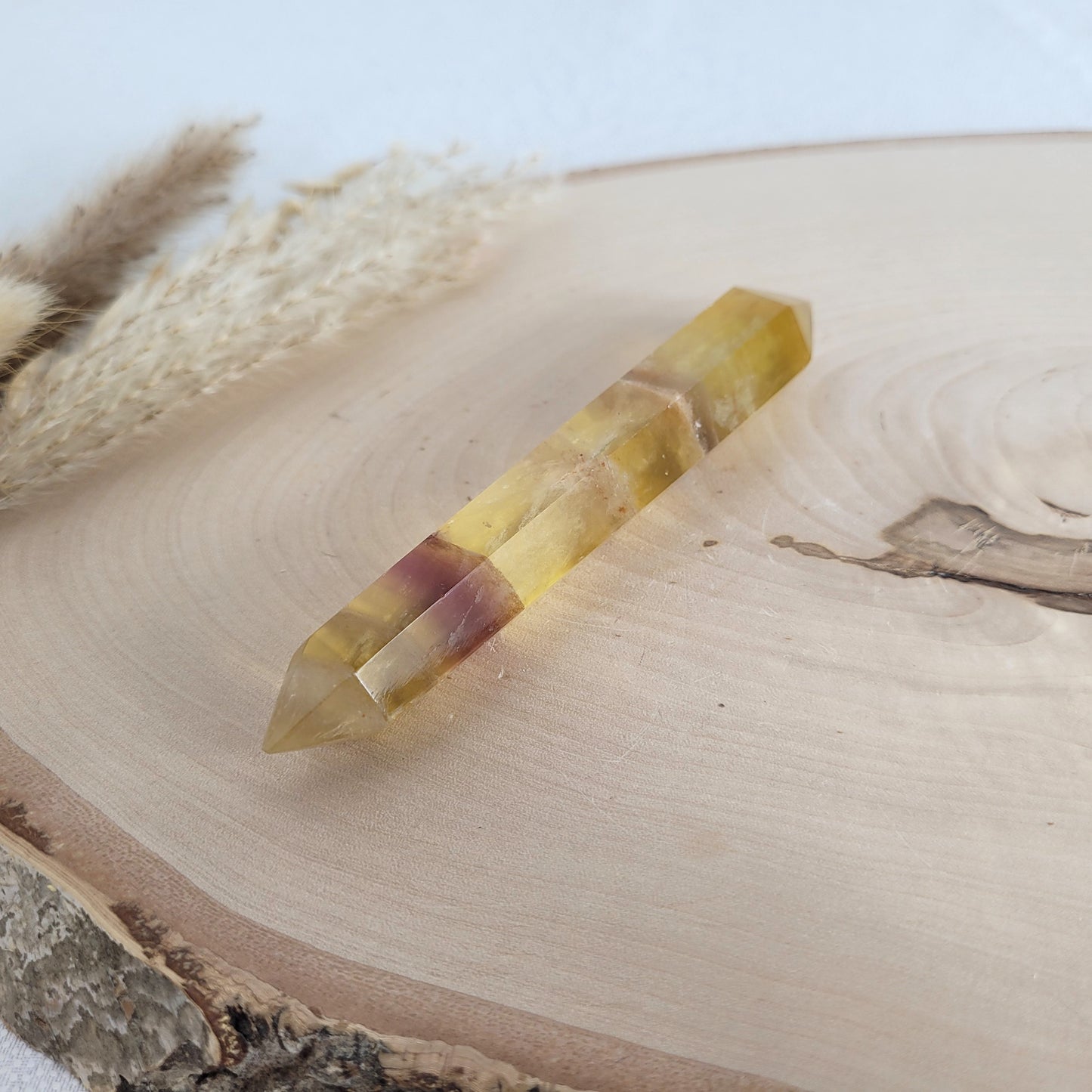 Geschliffener Fluorit Doppelender mit intensiver Farbbänderung und klarer Kristallstruktur, platziert auf einer Holzscheibe.