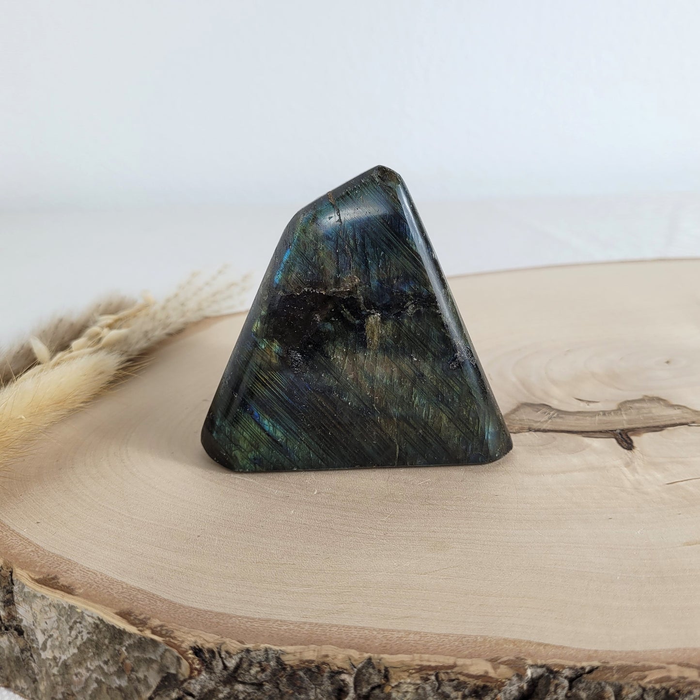 Labradorit Freiform mit natürlichem, intensivem Farbspiel, präsentiert auf einer Holzscheibe. Die typische Lamellenstruktur bricht das Licht auf besondere Weise und macht das Stück zu einem besonderen Blickfang.