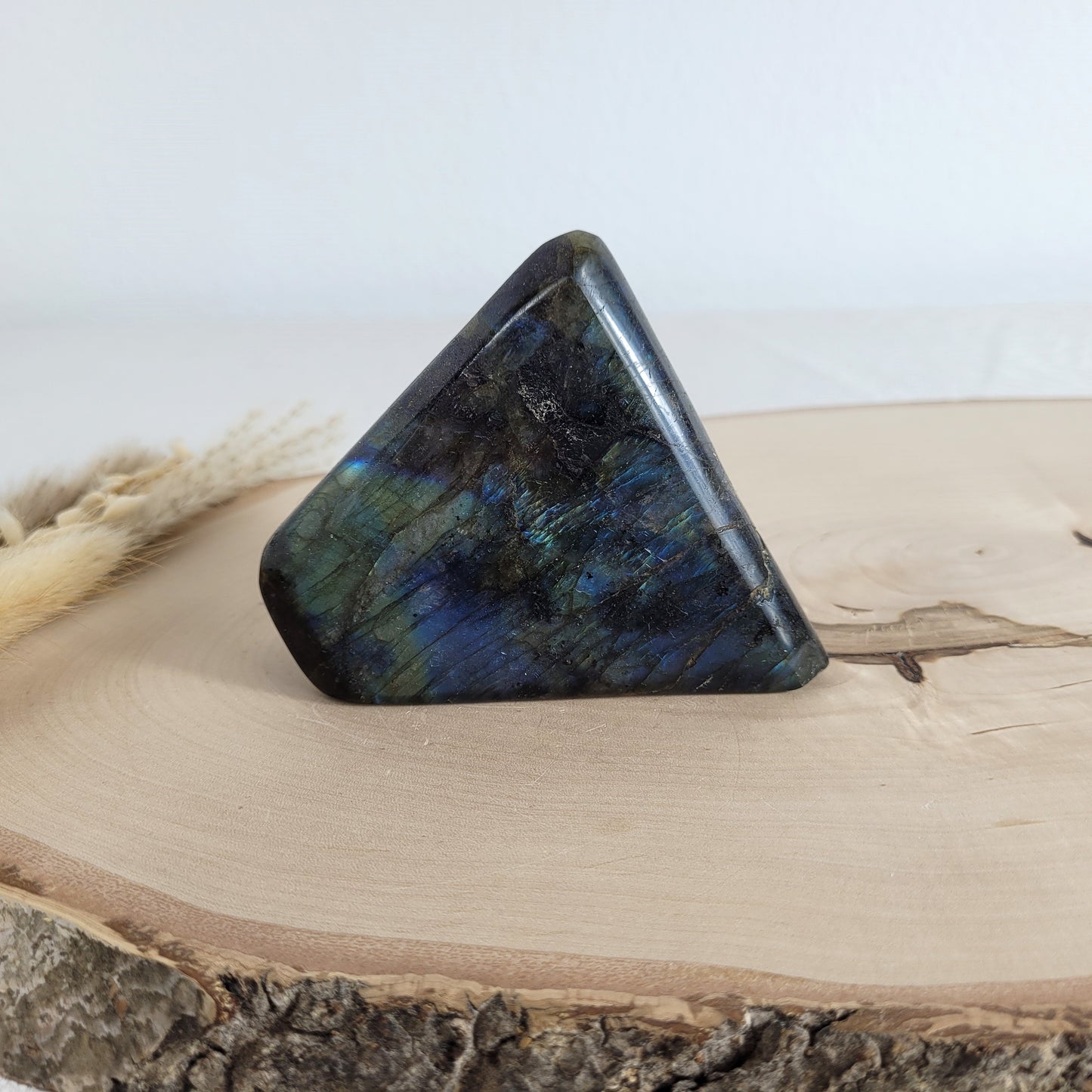 Labradorit Freiform mit natürlichem, intensivem Farbspiel, präsentiert auf einer Holzscheibe. Die typische Lamellenstruktur bricht das Licht auf besondere Weise und macht das Stück zu einem besonderen Blickfang.
