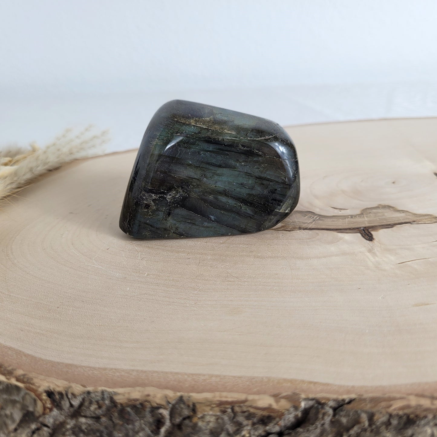 Labradorit Freiform mit natürlichem, intensivem Farbspiel, präsentiert auf einer Holzscheibe. Die typische Lamellenstruktur bricht das Licht auf besondere Weise und macht das Stück zu einem besonderen Blickfang.