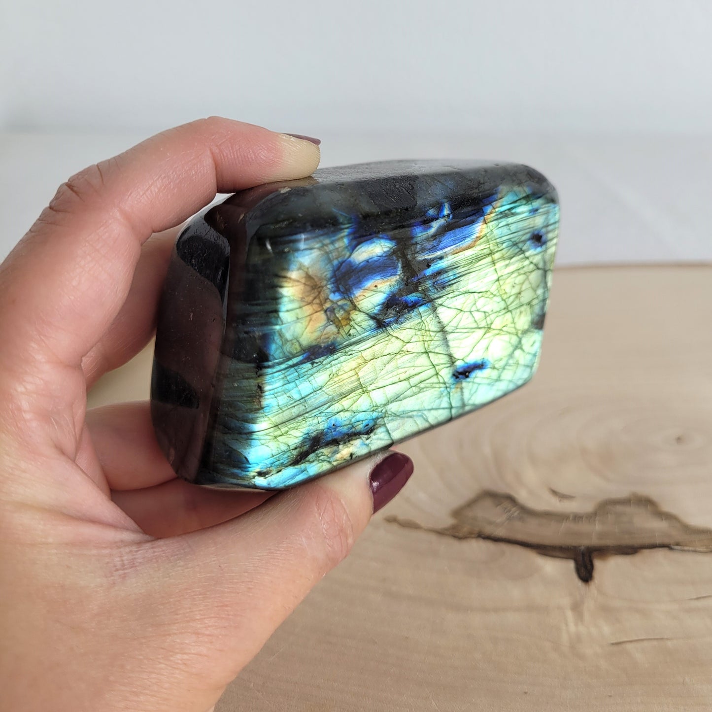 Labradorit Freiform mit natürlichem, intensivem Farbspiel, präsentiert auf einer Holzscheibe. Die typische Lamellenstruktur bricht das Licht auf besondere Weise und macht das Stück zu einem besonderen Blickfang.