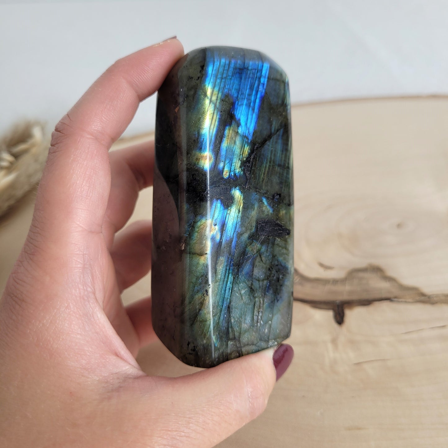 Labradorit Freiform mit natürlichem, intensivem Farbspiel, präsentiert auf einer Holzscheibe. Die typische Lamellenstruktur bricht das Licht auf besondere Weise und macht das Stück zu einem besonderen Blickfang.