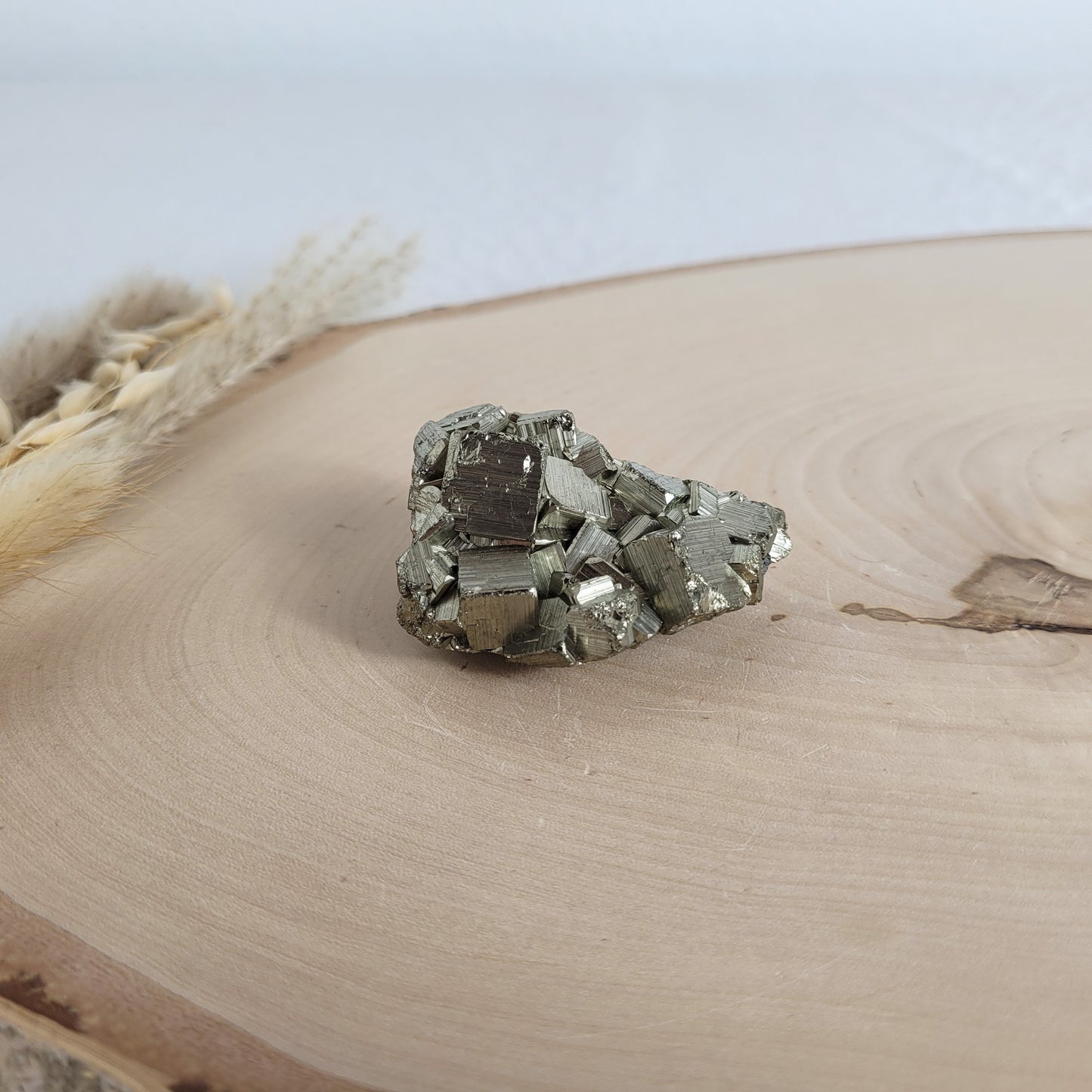 Pyrit-Kristallstufe auf einer Holzscheibe als natürlicher Hintergrund. Die metallisch glänzenden Kristalle heben sich kontrastreich vom warmen Holzton ab.