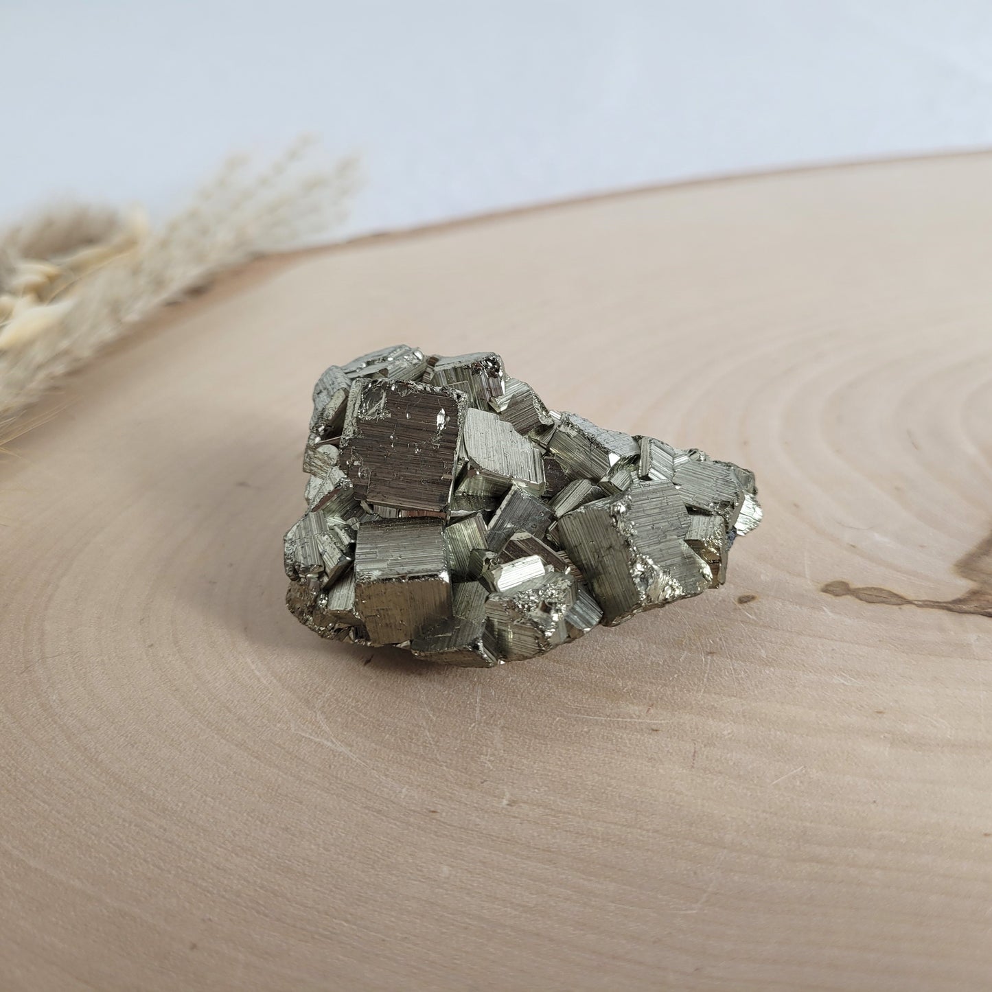 Pyrit-Kristallstufe auf einer Holzscheibe als natürlicher Hintergrund. Die metallisch glänzenden Kristalle heben sich kontrastreich vom warmen Holzton ab.