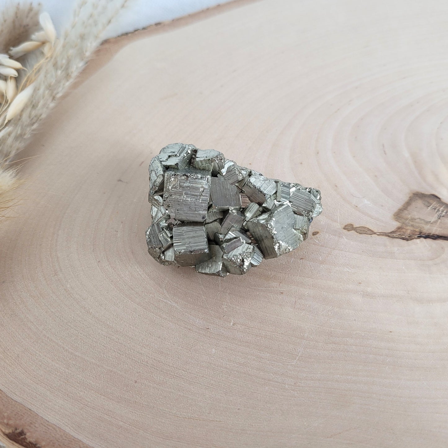 Pyrit-Kristallstufe auf einer Holzscheibe als natürlicher Hintergrund. Die metallisch glänzenden Kristalle heben sich kontrastreich vom warmen Holzton ab.
