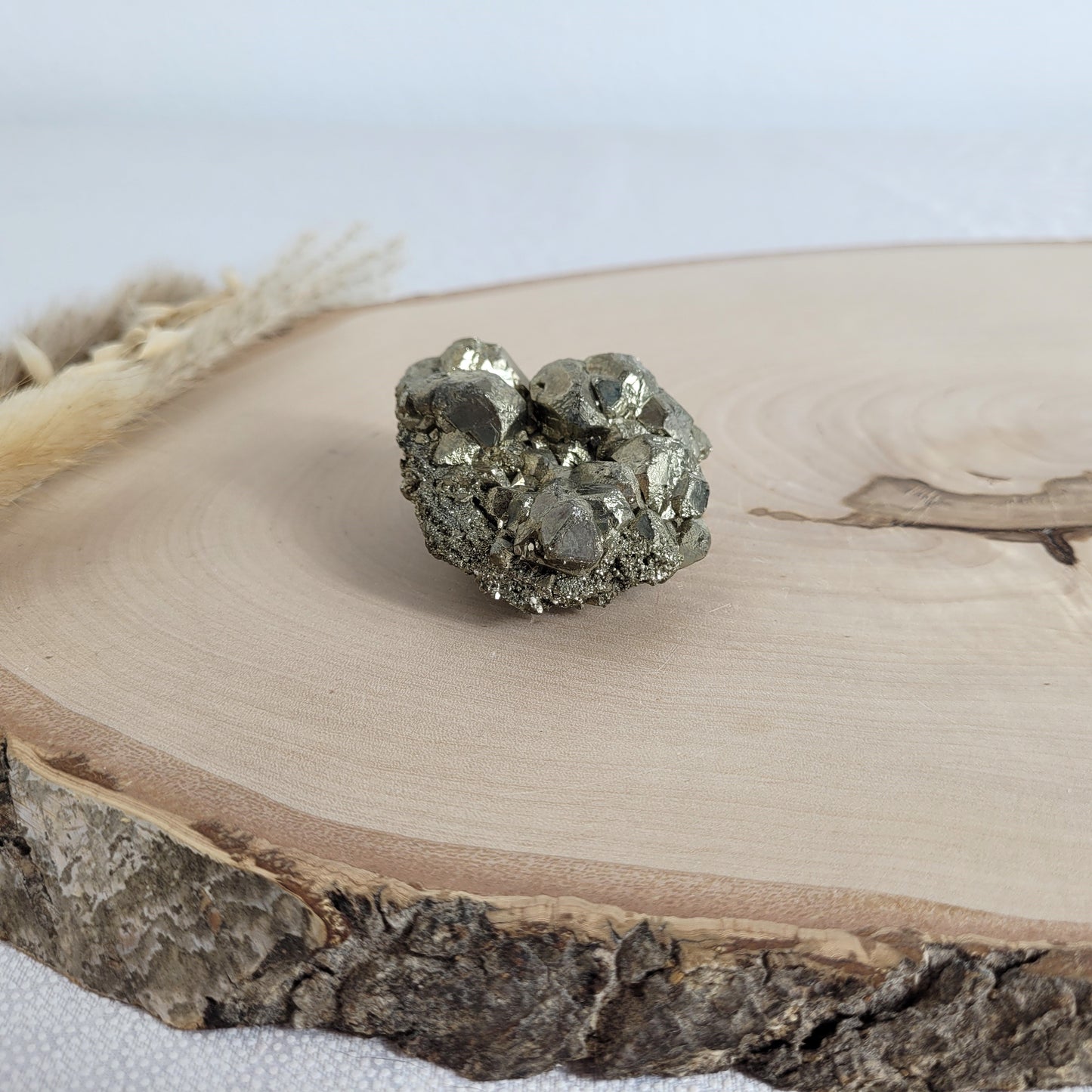 Pyrit-Kristallstufe auf einer Holzscheibe als natürlicher Hintergrund. Die metallisch glänzenden Kristalle heben sich kontrastreich vom warmen Holzton ab.