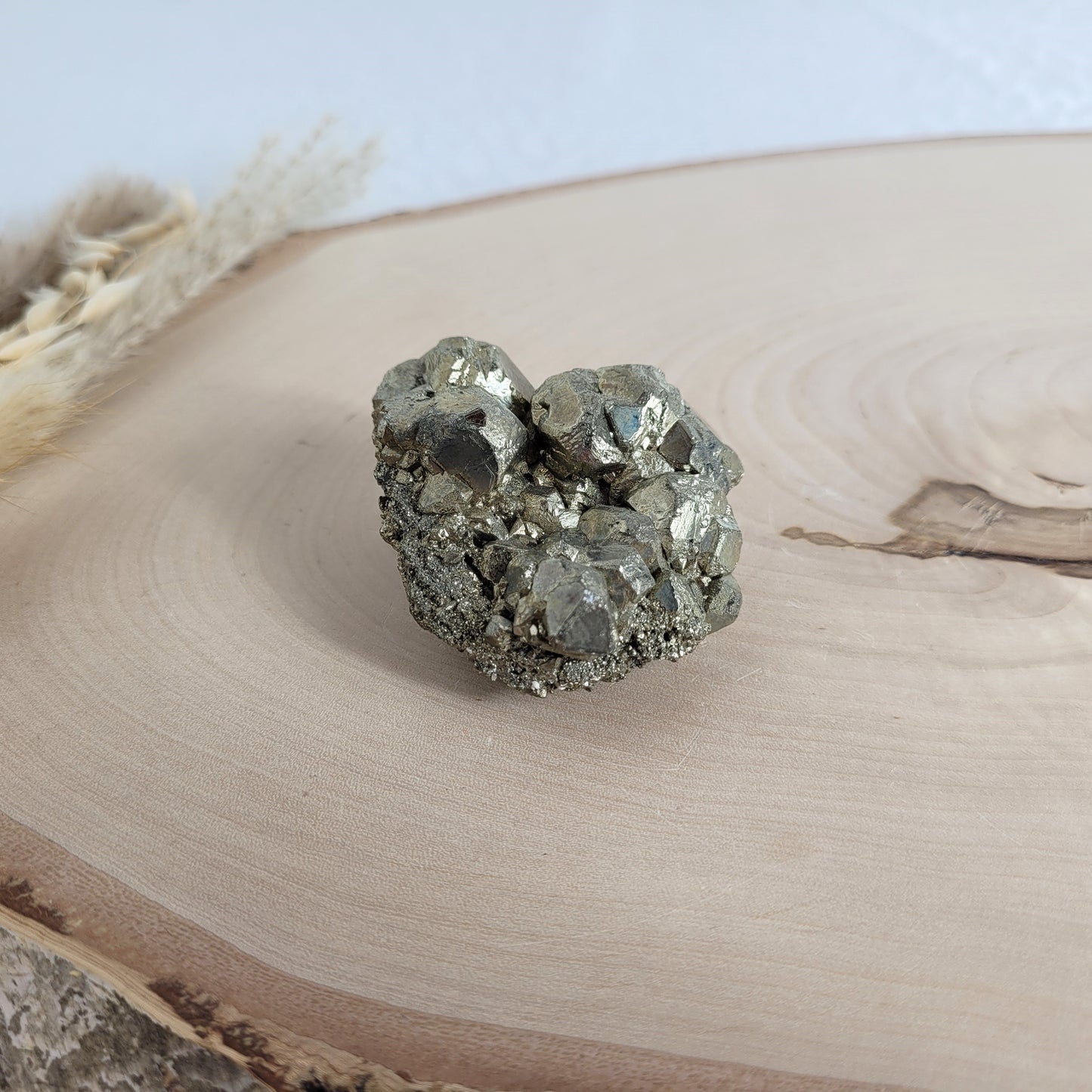Pyrit-Kristallstufe auf einer Holzscheibe als natürlicher Hintergrund. Die metallisch glänzenden Kristalle heben sich kontrastreich vom warmen Holzton ab.