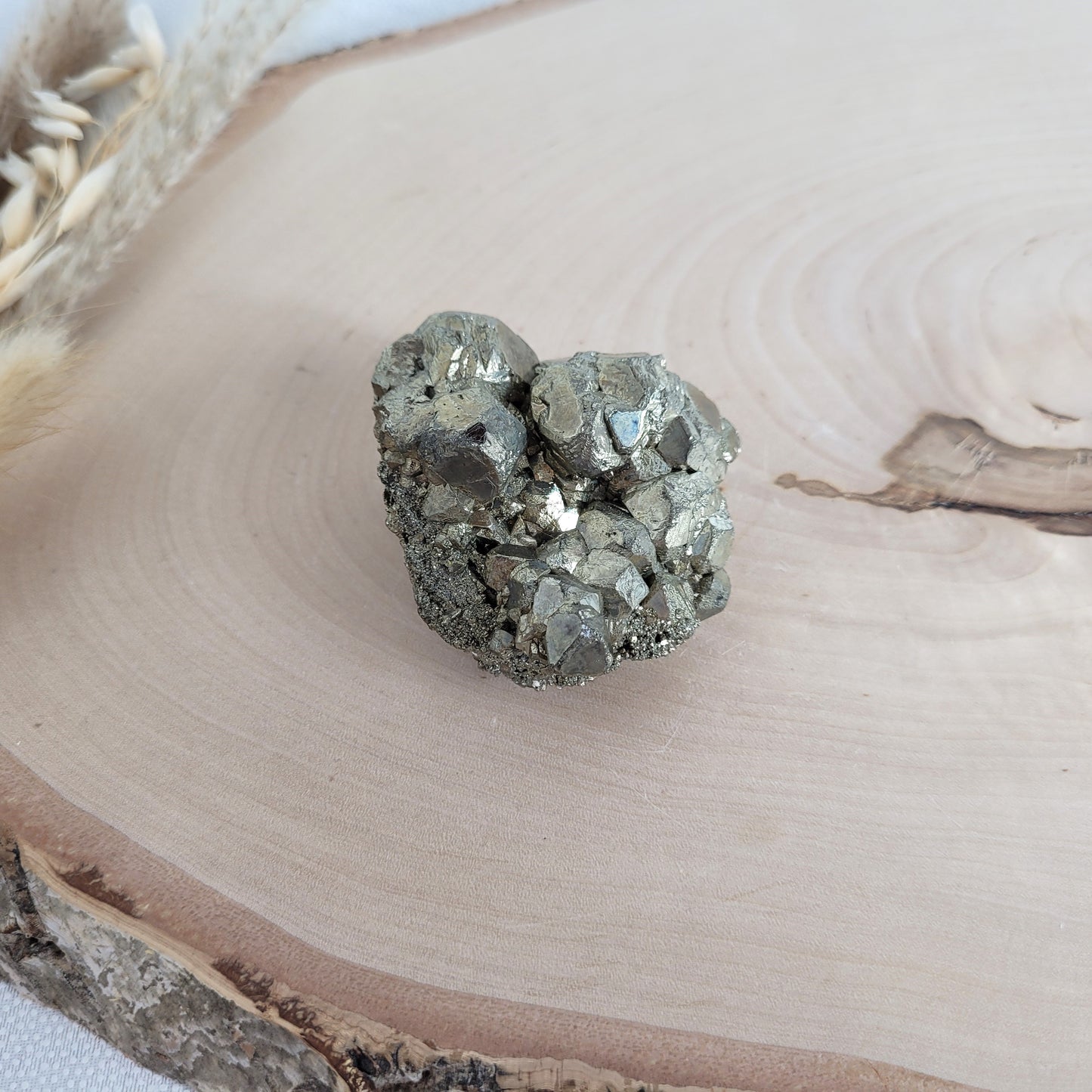 Pyrit-Kristallstufe auf einer Holzscheibe als natürlicher Hintergrund. Die metallisch glänzenden Kristalle heben sich kontrastreich vom warmen Holzton ab.