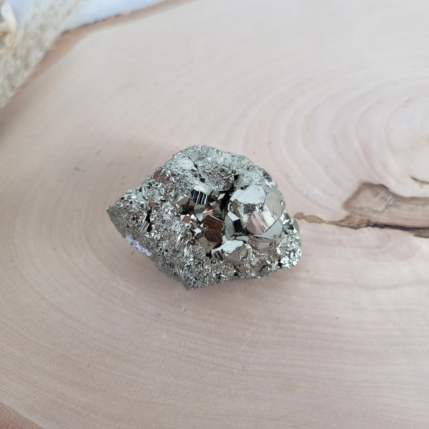 Pyrit-Kristallstufe auf einer Holzscheibe als natürlicher Hintergrund. Die metallisch glänzenden Kristalle heben sich kontrastreich vom warmen Holzton ab.