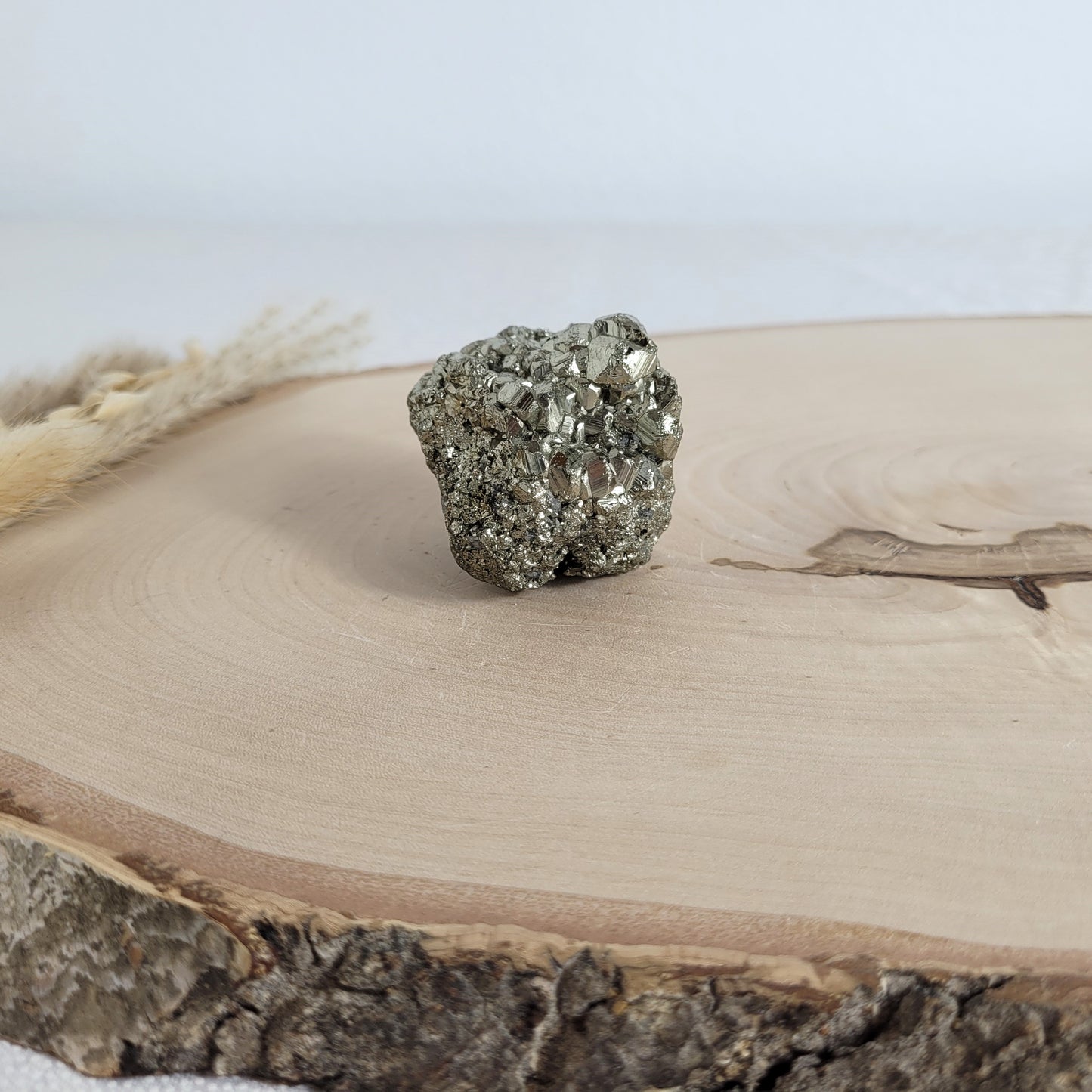 Pyrit-Kristallstufe auf einer Holzscheibe als natürlicher Hintergrund. Die metallisch glänzenden Kristalle heben sich kontrastreich vom warmen Holzton ab.